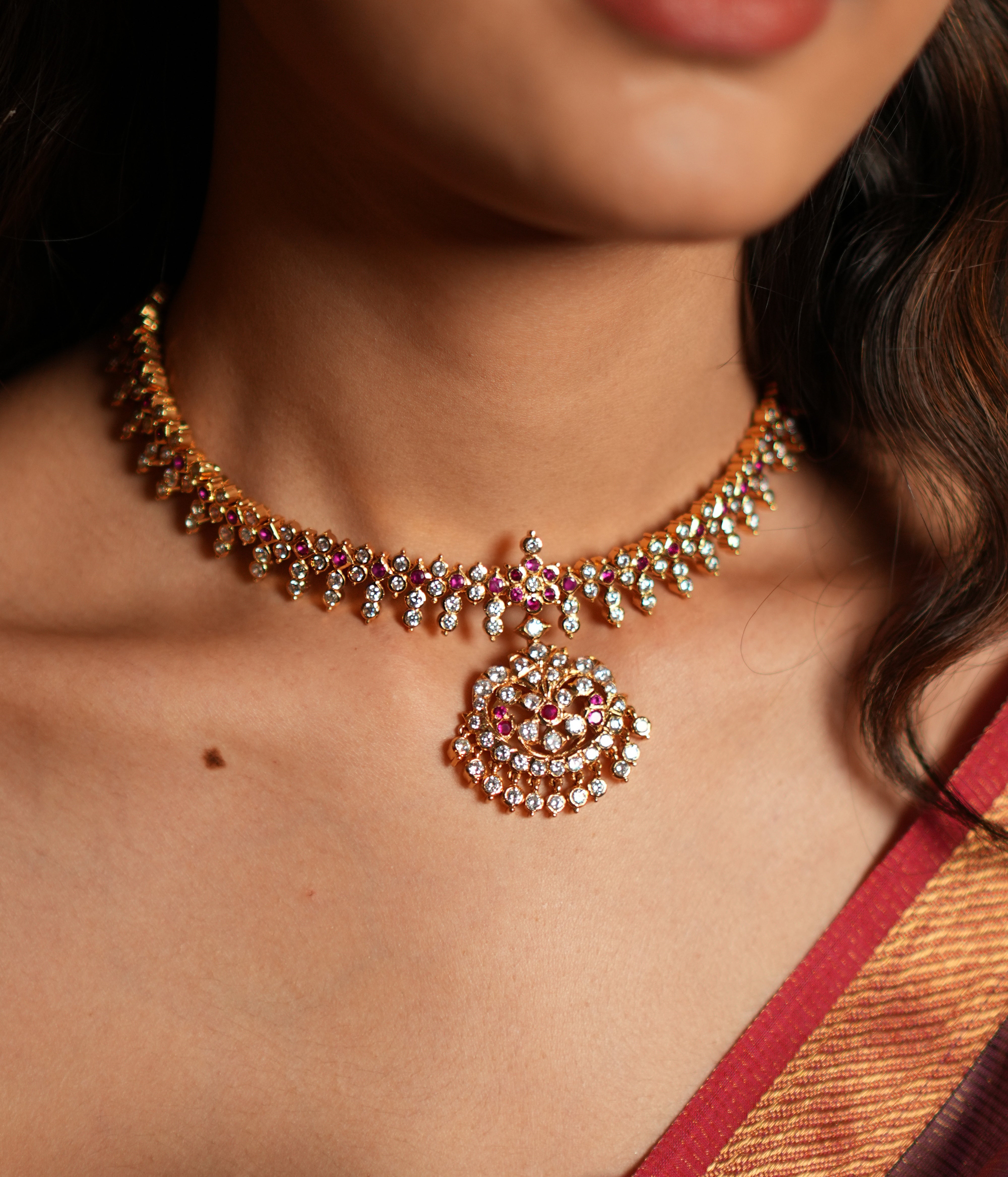 Elevate your traditional attire with this exquisite Attigai necklace, crafted from 92.5 sterling silver and finished with a rich 22-carat gold plating. Adorned with dazzling Swarovski crystals and accented with vivid pink gemstones, this necklace exudes timeless elegance and sophistication. 