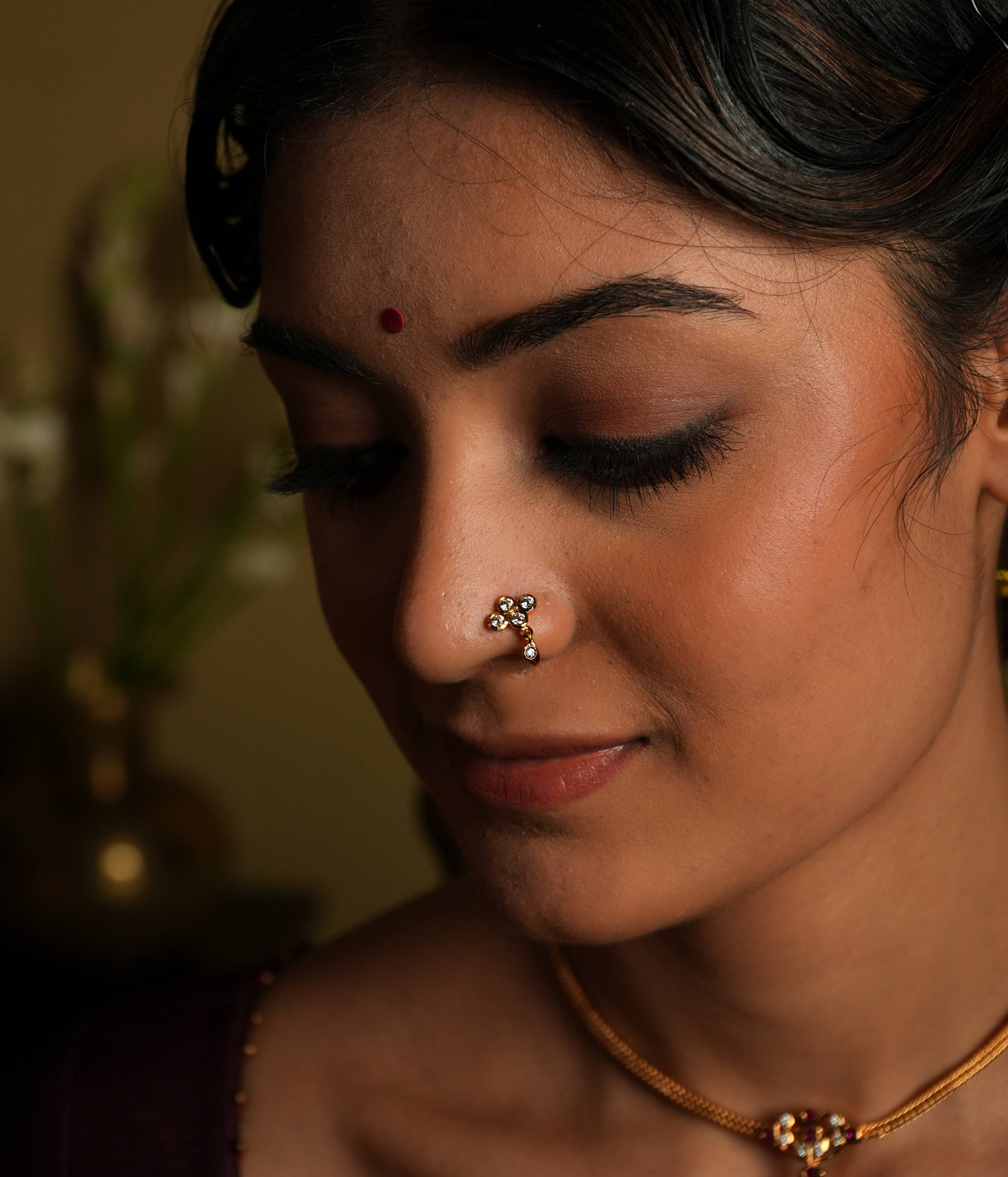 92.5 silver gold plated. This minimal nose stud shines with understated elegance,
featuring a moissanite set stone. A dangling moissanite drop adds a touch of delicate charm,
inspired by vintage Chettinad design language. A tiny, timeless treasure that exudes refined
sophistication.