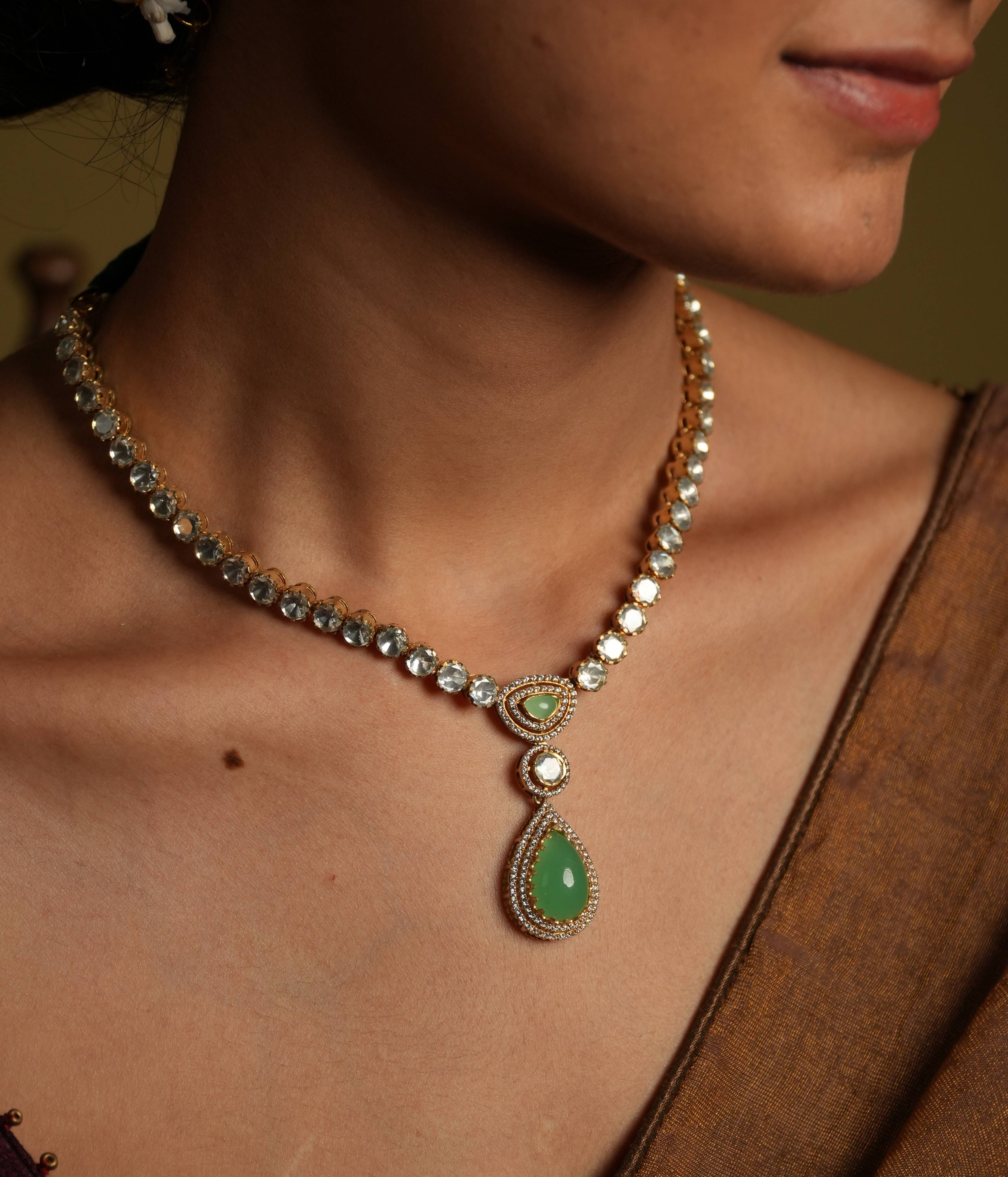 92.5 silver with gold plating This minimal yet statement polki set necklace
shines with sleek sophistication, arranged in a single line. A green gemstone teardrop
pendant, lined with moissanite, adds a touch of luxurious whimsy, creating a truly
show-stopping piece