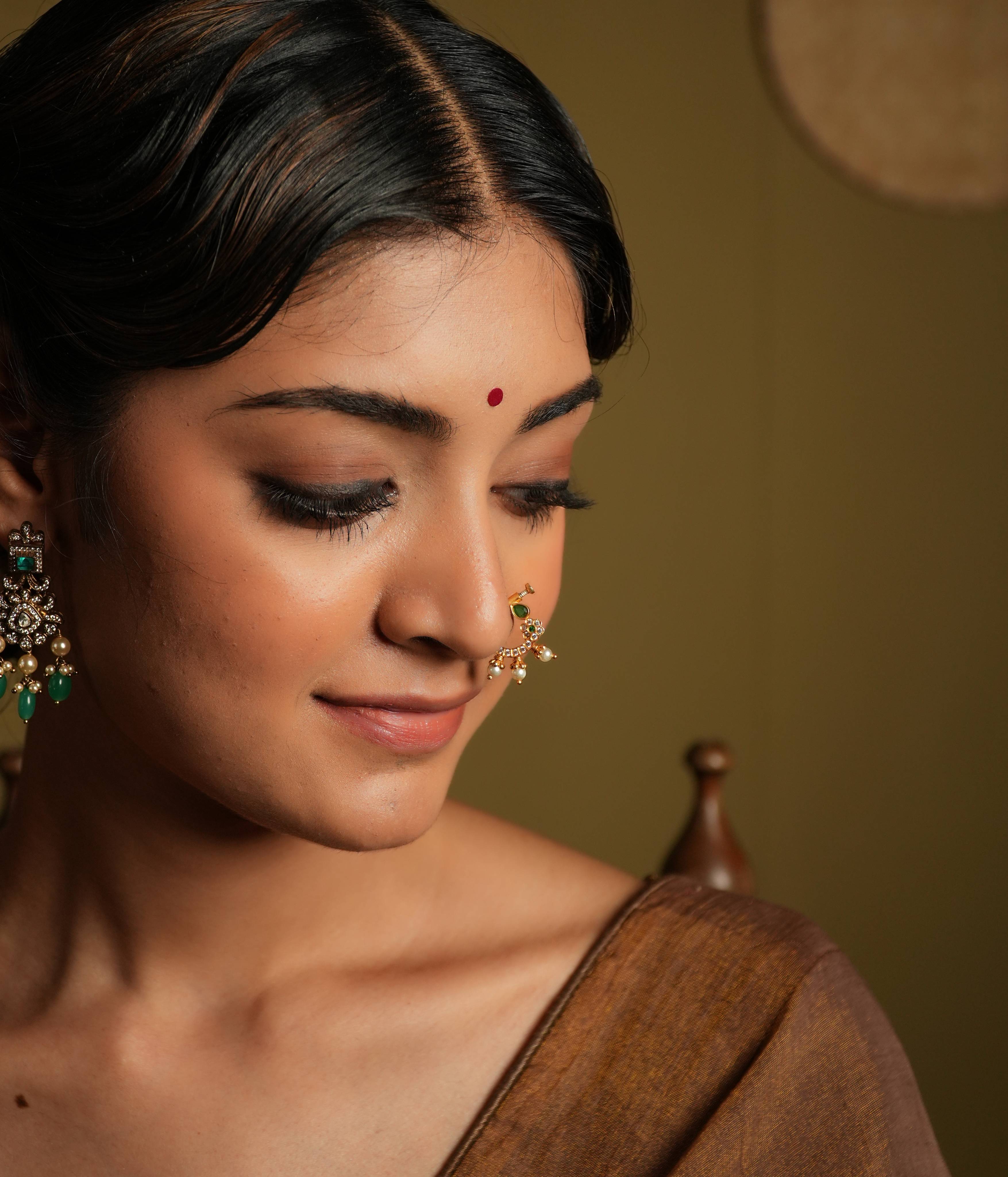 This gold plated silver nose ring shines with delicate
elegance, featuring a white Kundan setting and minimal stone set flower motif. Three bold
pearl edgings add a touch of luxurious sophistication, evoking the rich heritage of Indian
craftsmanship.