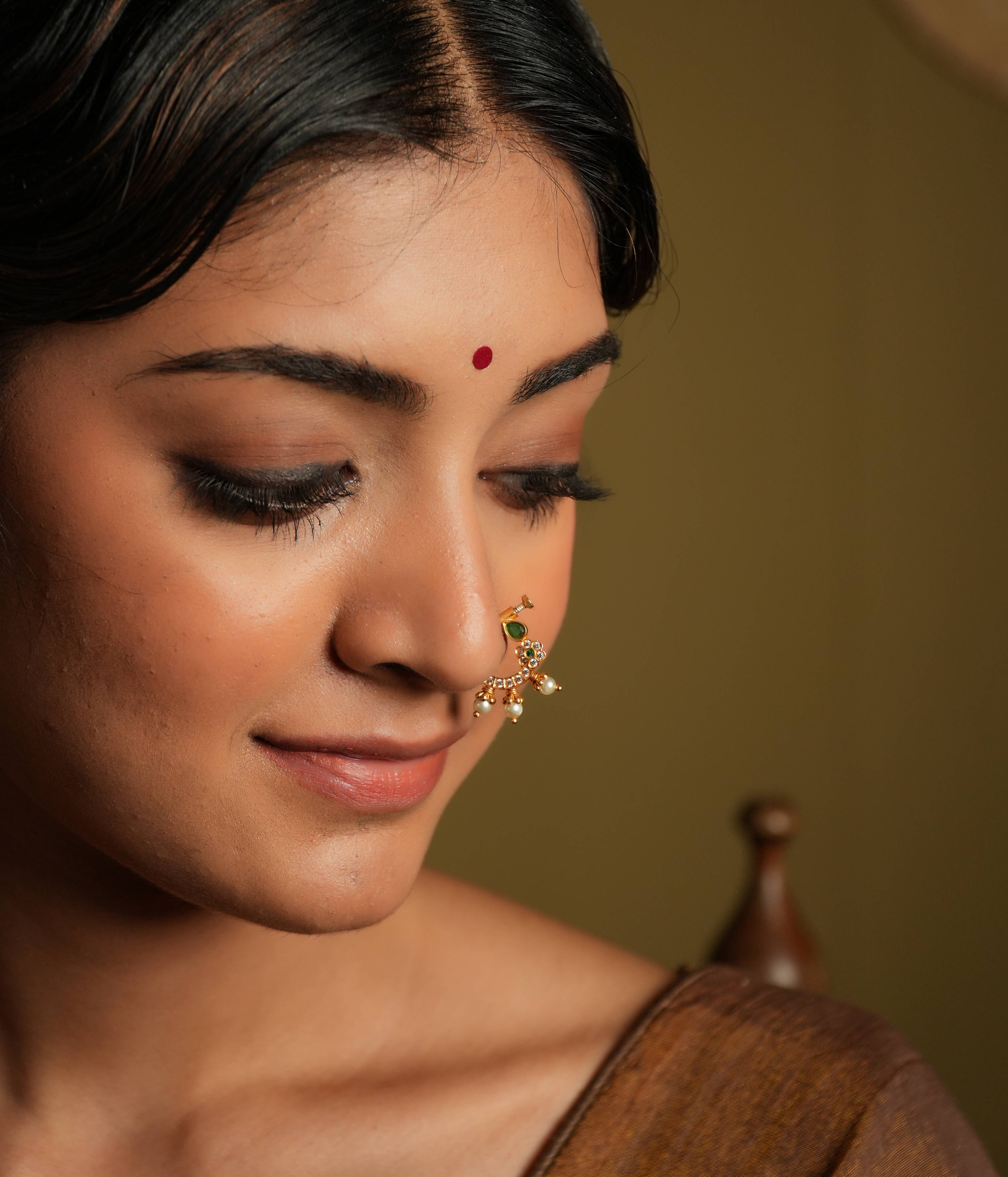 This gold plated silver nose ring shines with delicate
elegance, featuring a white Kundan setting and minimal stone set flower motif. Three bold
pearl edgings add a touch of luxurious sophistication, evoking the rich heritage of Indian
craftsmanship.