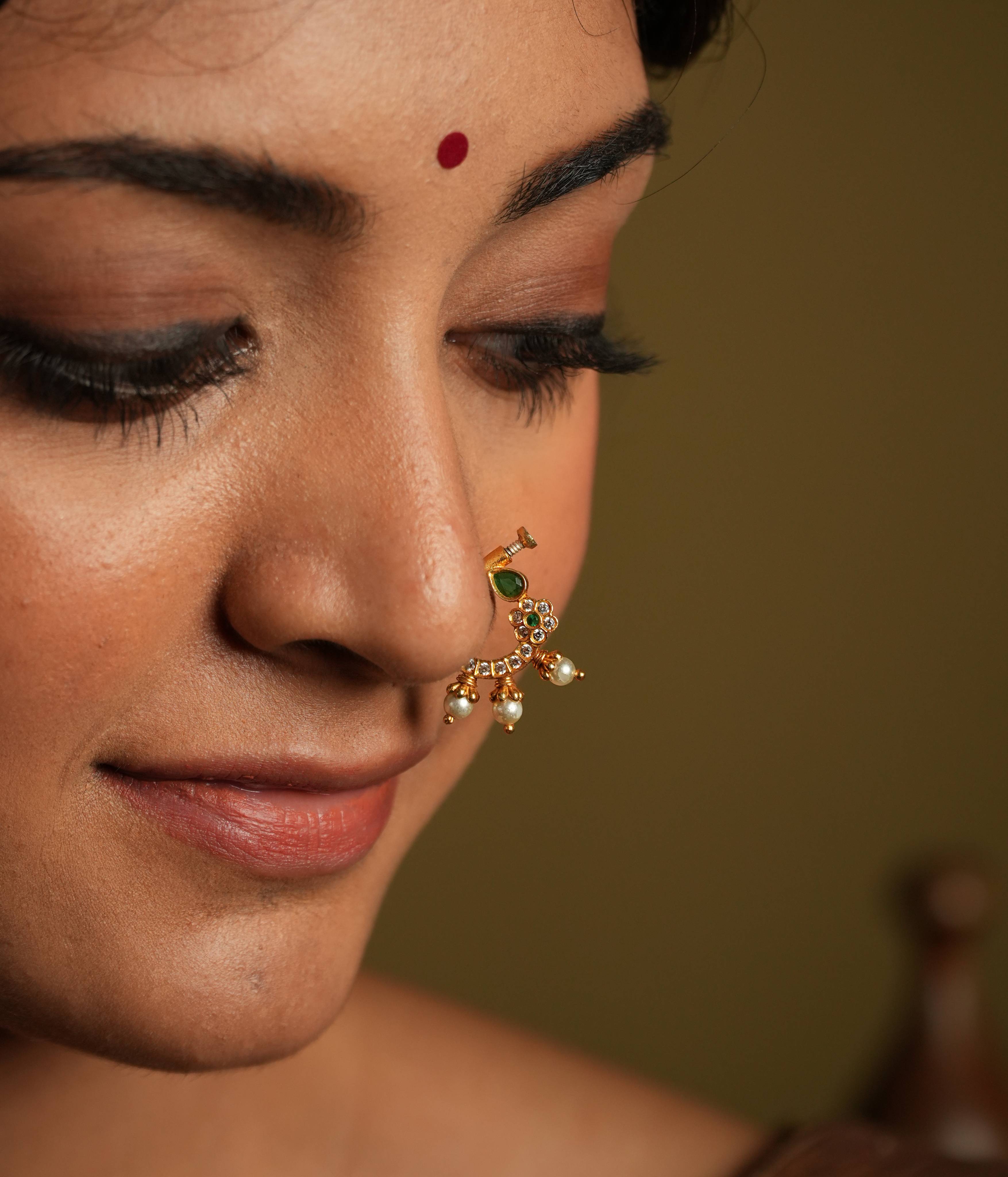 This gold plated silver nose ring shines with delicate
elegance, featuring a white Kundan setting and minimal stone set flower motif. Three bold
pearl edgings add a touch of luxurious sophistication, evoking the rich heritage of Indian
craftsmanship.