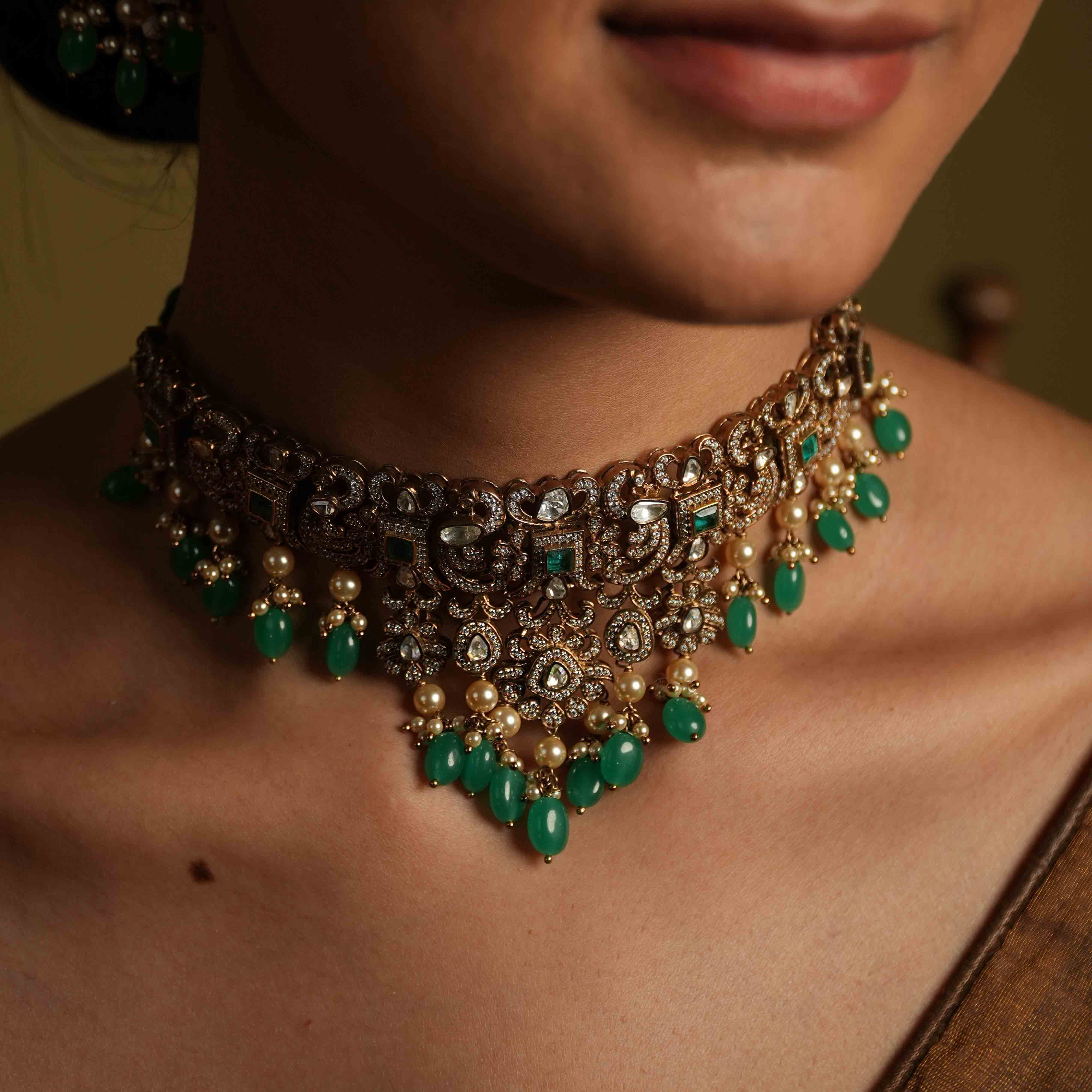 A handcrafted 92.5 sterling silver and 14ct dark antique gold plated choker, featuring moissanite, CZ stones, polki stones, and green spinel stones, finished in a Victorian style, with delicate pearl dangles, evoking regal romance and the opulence of a bygone era.