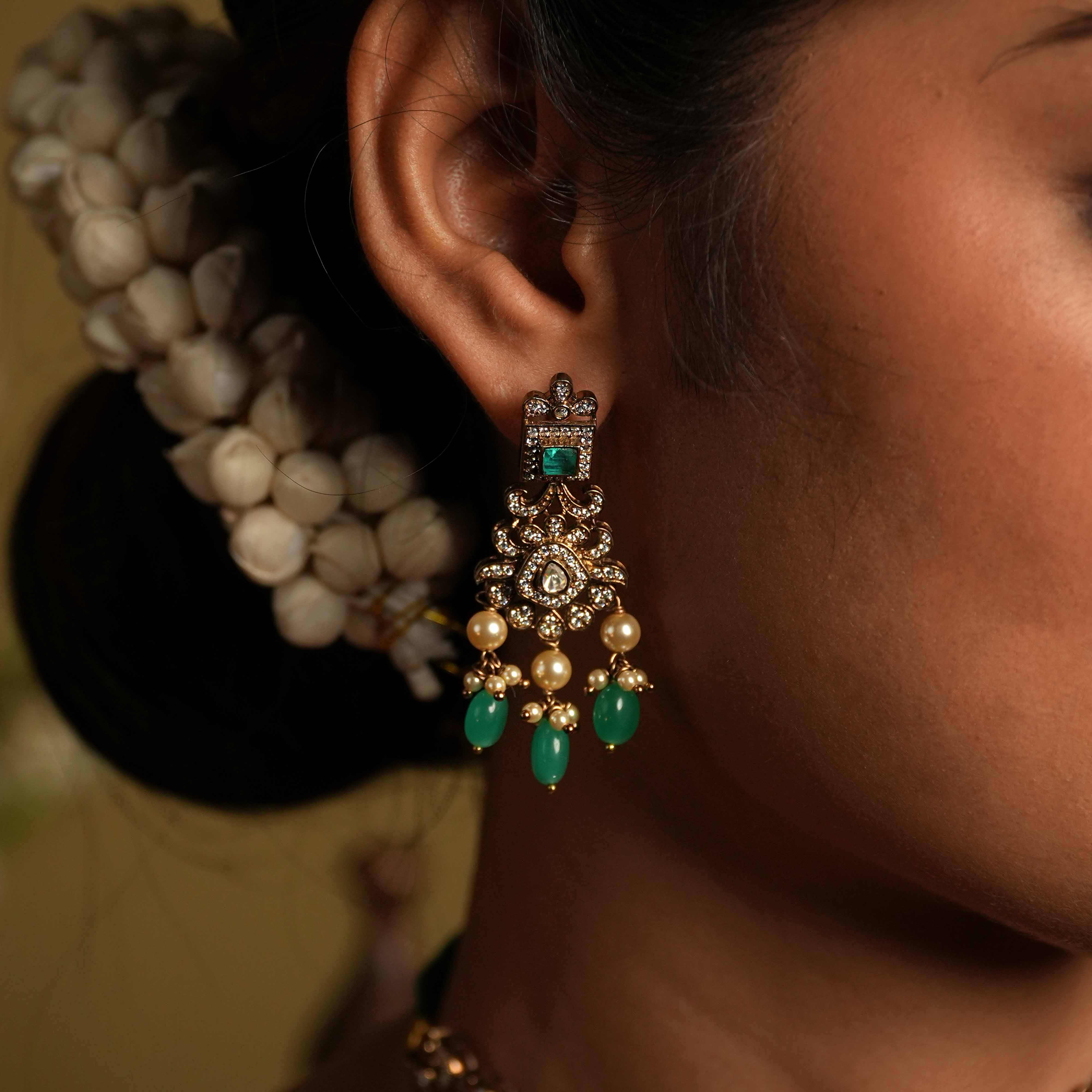 These intricate drop earrings, crafted from 92.5 sterling silver and featuring Bombay screw fastenings, showcase moissanite and bold green gemstones, complemented by delicate pearl dangles that evoke the opulence of a Victorian era.