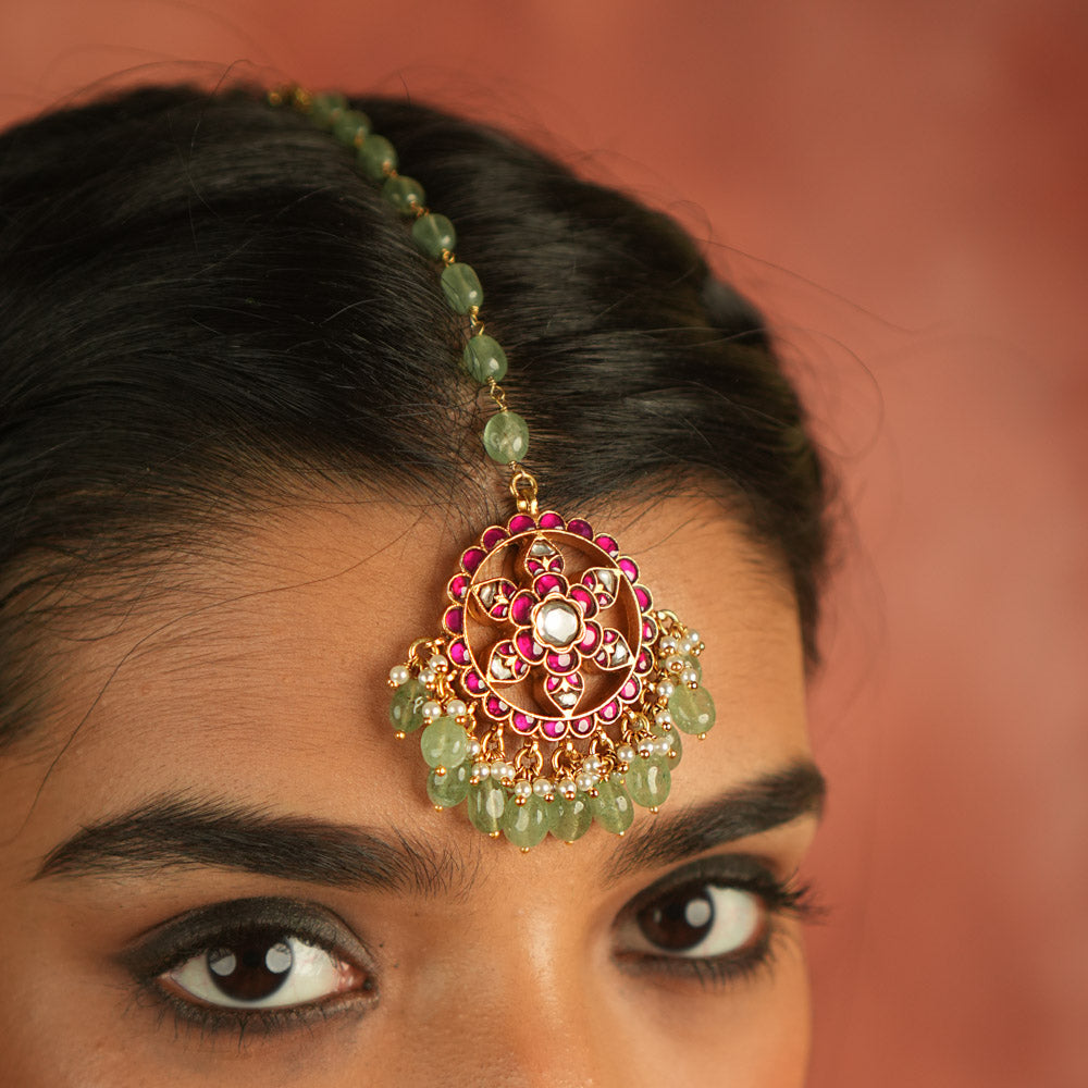 A symbol of blossoming beauty, this maangtika features a stunning combination of red Kundan stones, white Kundan stones, green beads, and pearls. With its romantic allure and vibrant green accents, it is a timeless treasure for the modern bride.