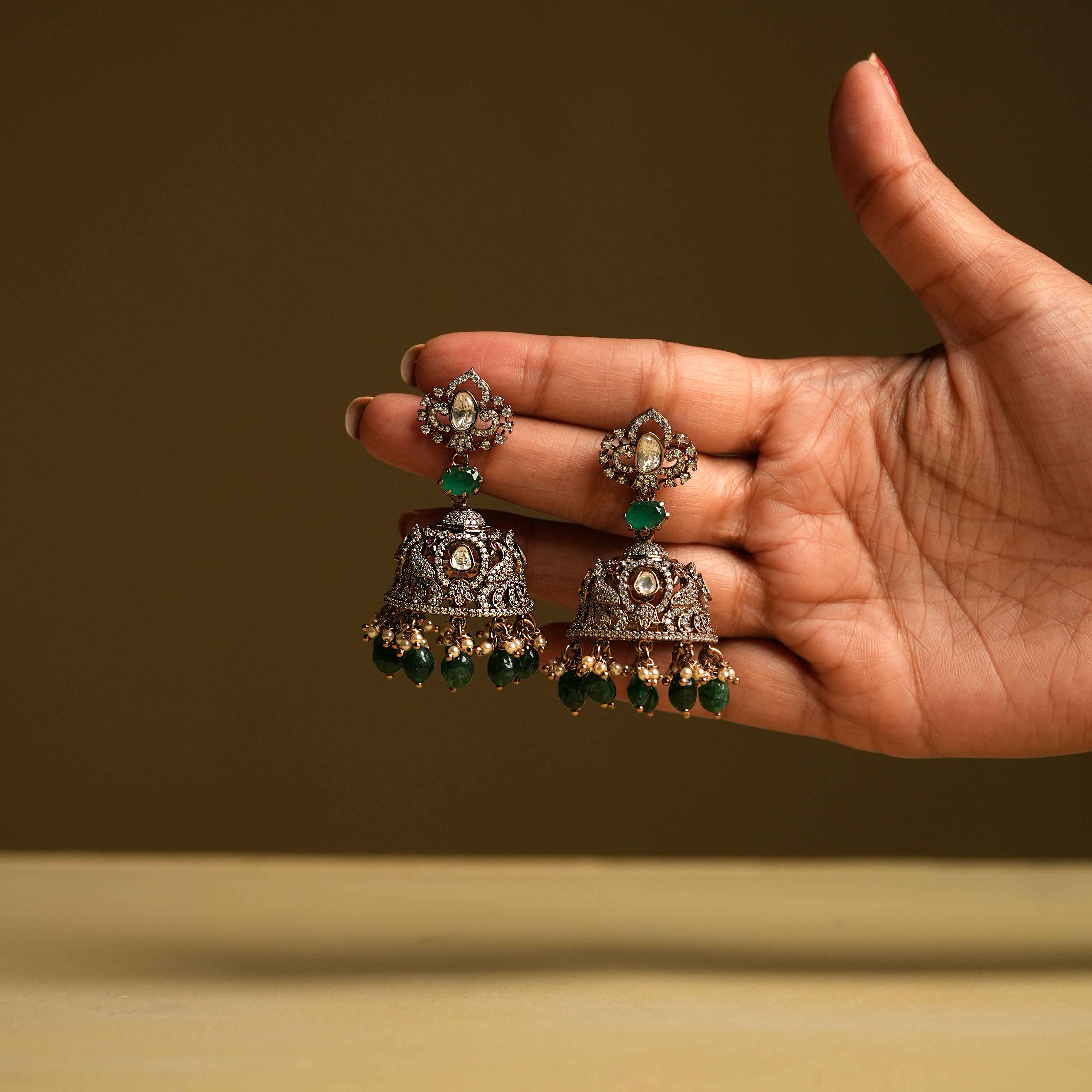 Ethereal moissanite jhumkas, handcrafted from 92.5 sterling silver with 14ct dark antique gold plating and screw fastenings, feature green gemstones, polki stones, CZ stones, pearls, and green beads, accented with cultured emerald and pearl dangles in a Victorian-inspired design.