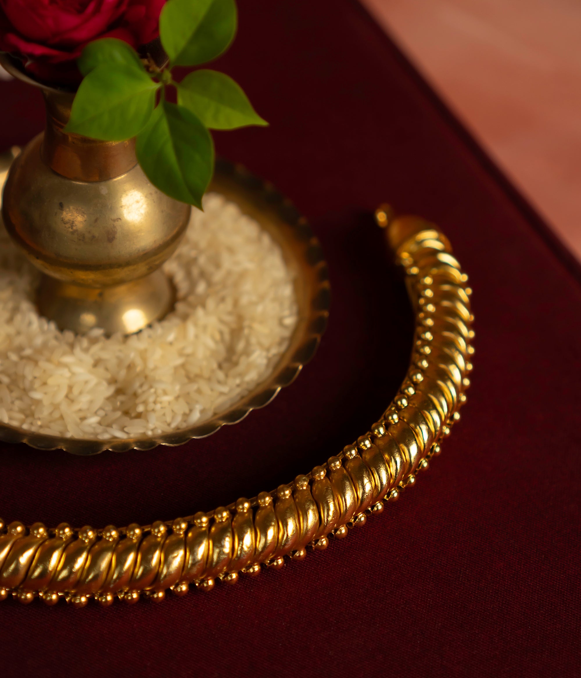 Gold necklace on a red surface with a small brass container and green leaves.