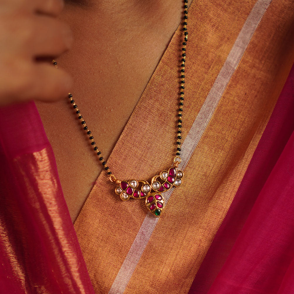 The Alagini Mangalsutra, crafted in gold-plated silver, features vibrant green and pink Kundan stones, beautifully complemented by traditional black beads. A perfect fusion of heritage and elegance, this piece embodies timeless charm with a contemporary touch.