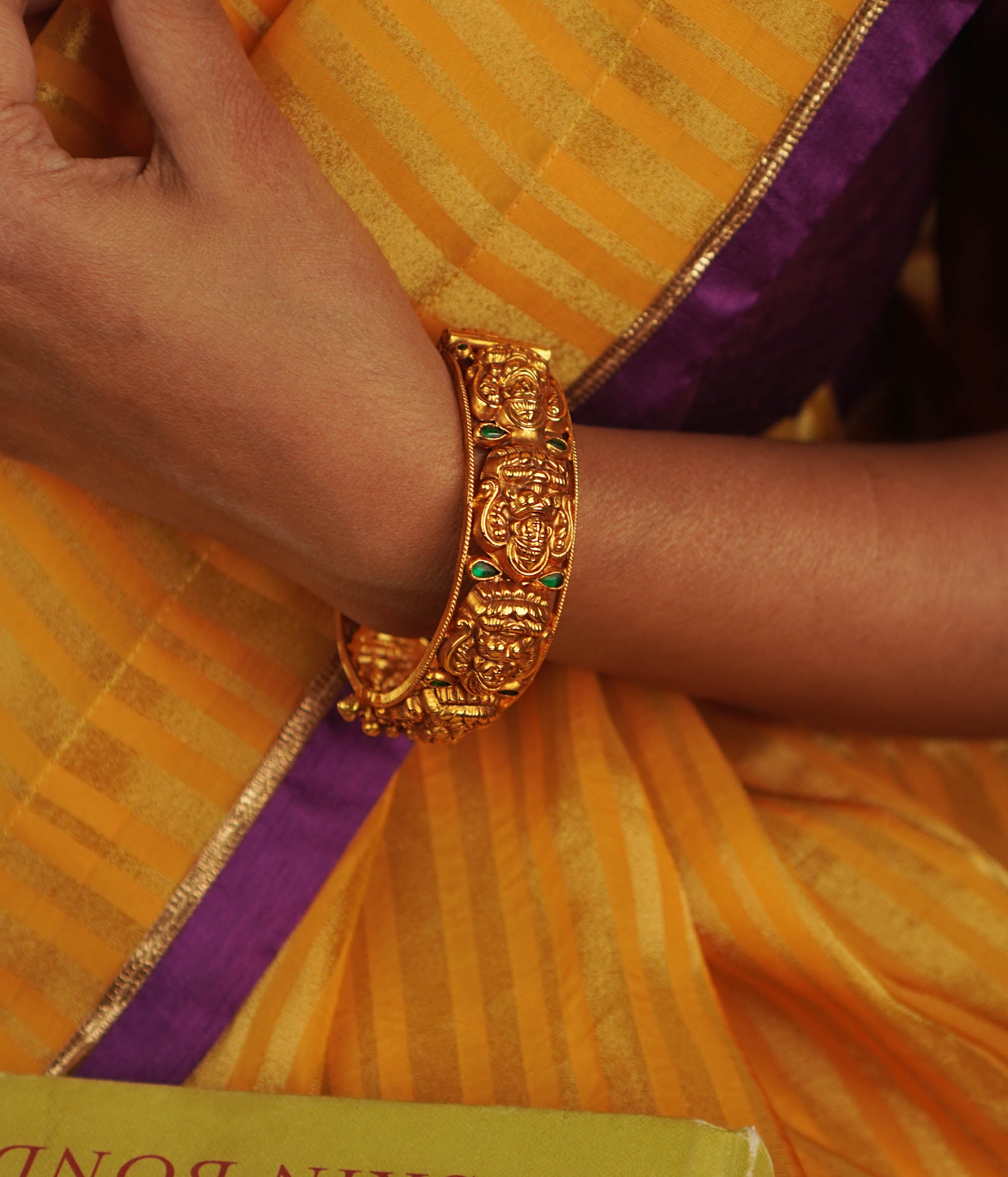 Antique gold-toned bangle featuring green kundan stones and engraved deities.