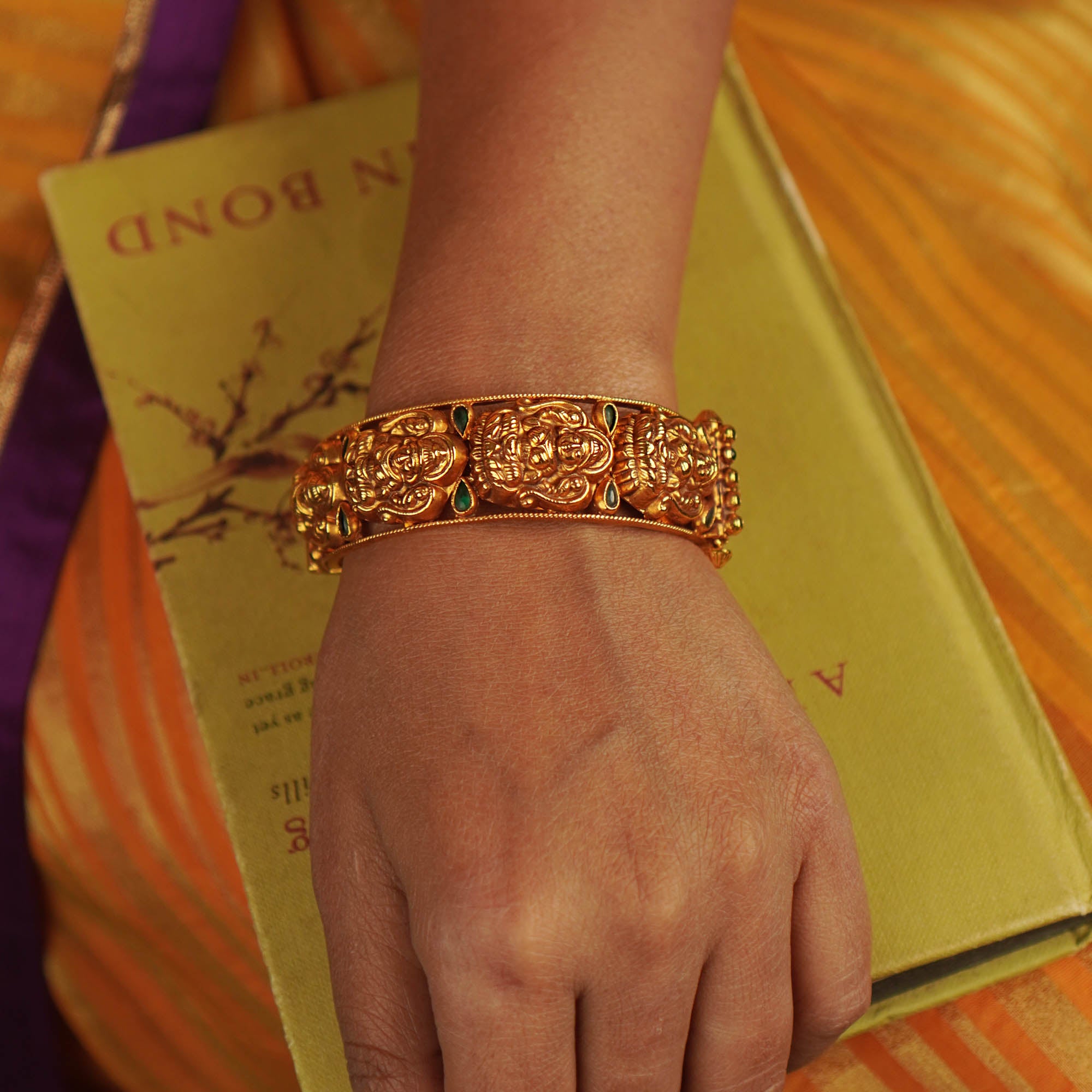 Antique gold-toned bangle featuring green kundan stones and engraved deities.