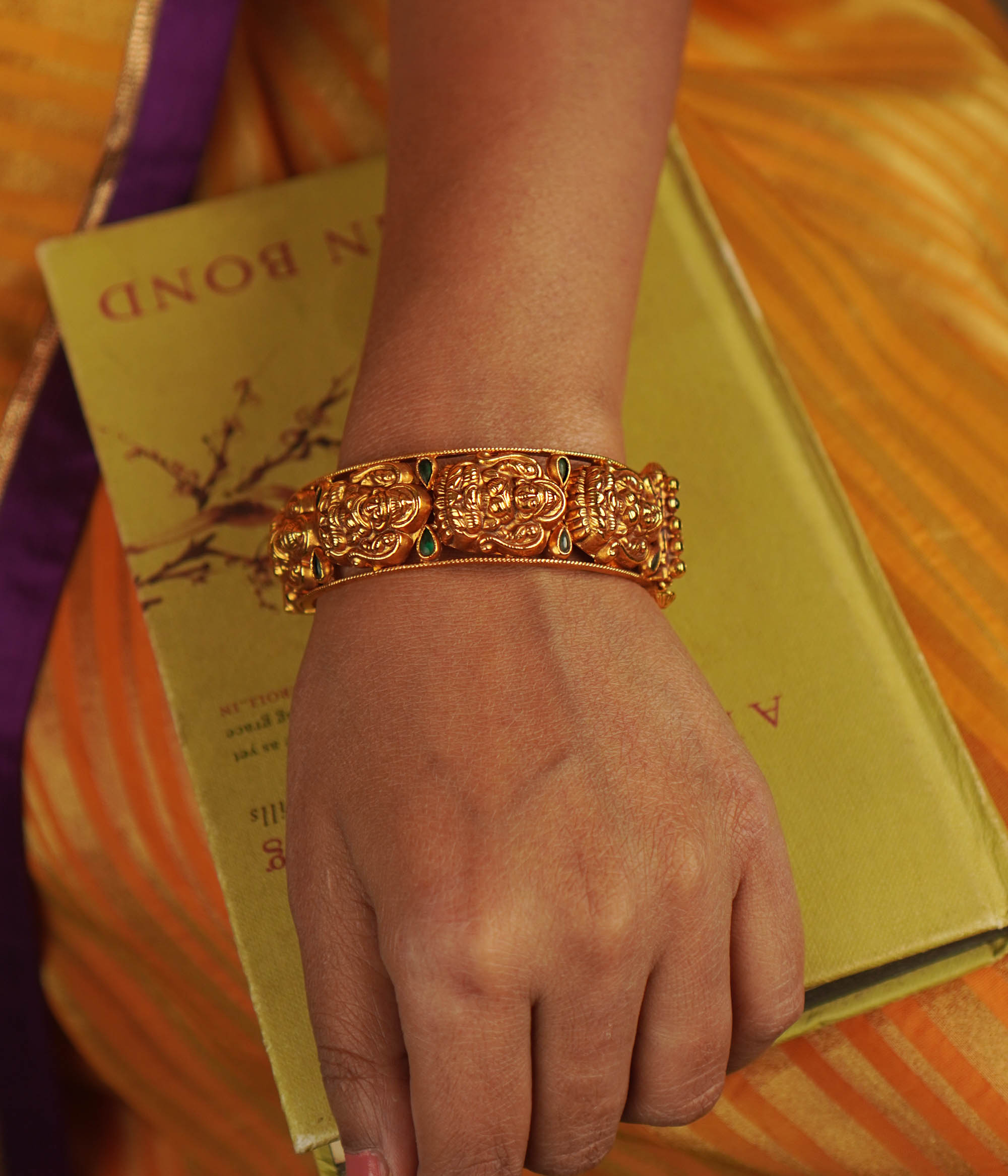 Antique gold-toned bangle featuring green kundan stones and engraved deities.