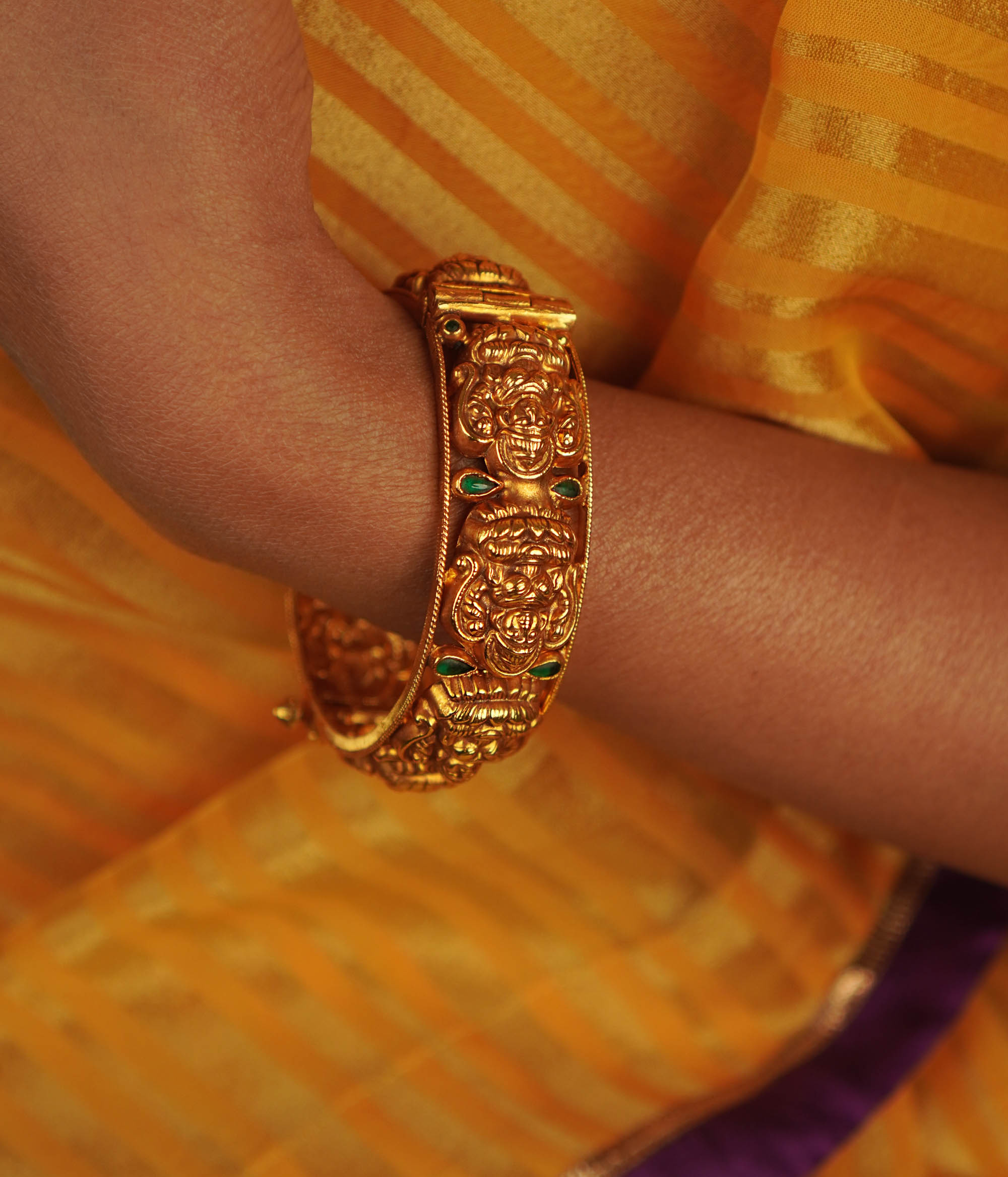 Antique gold-toned bangle featuring green kundan stones and engraved deities.