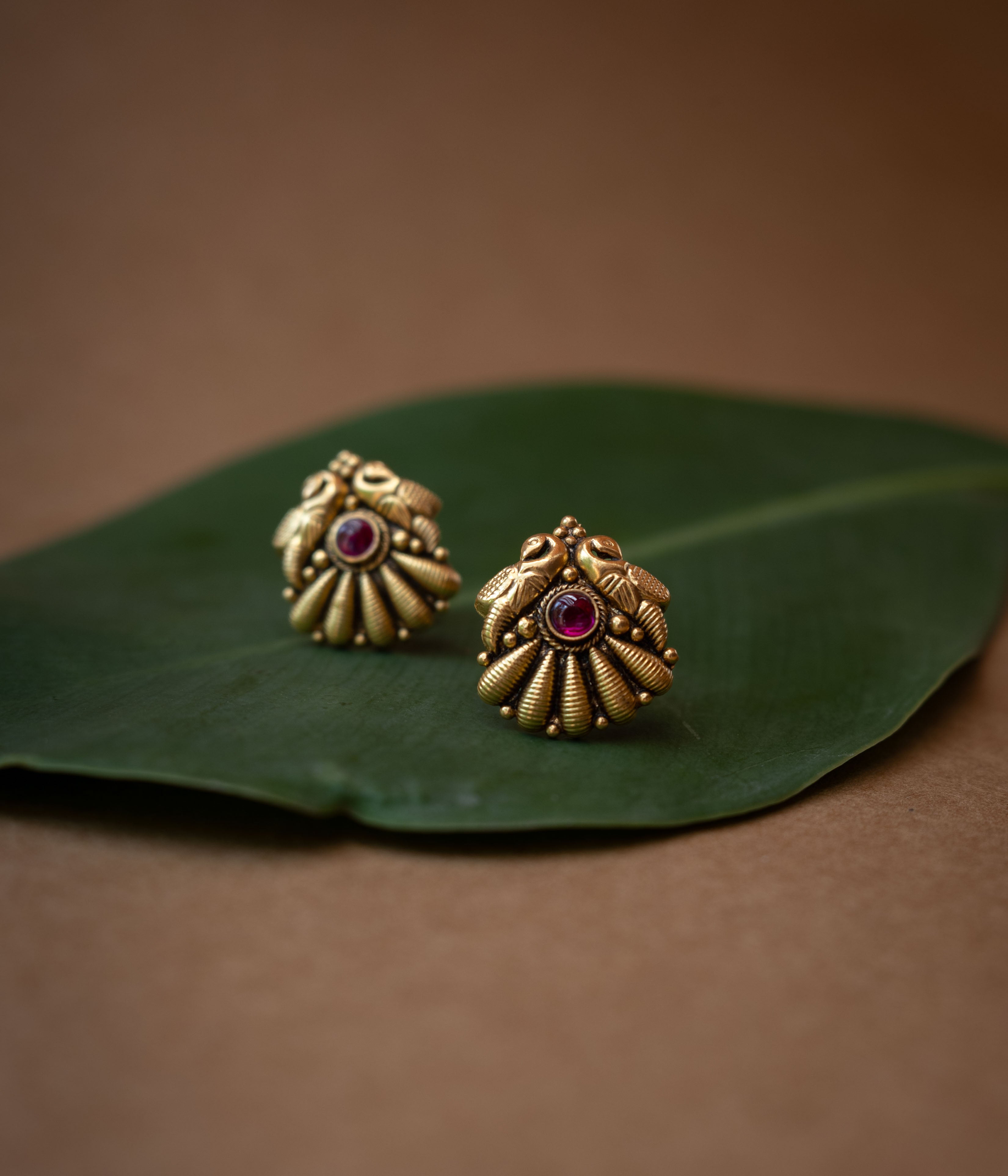 Traditional stud earrings with a central red stone and a stylized peacock and fan design.