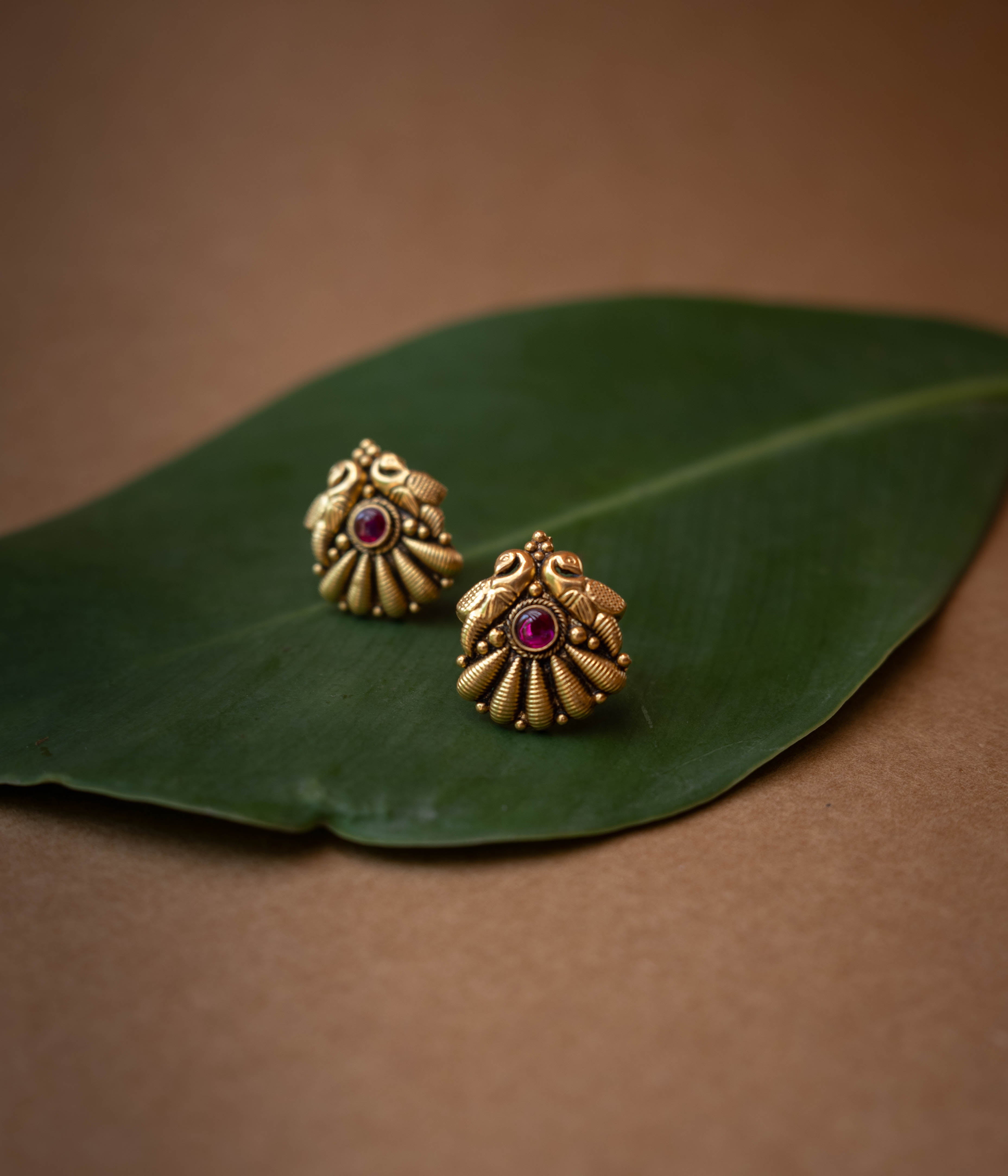Traditional stud earrings with a central red stone and a stylized peacock and fan design.
