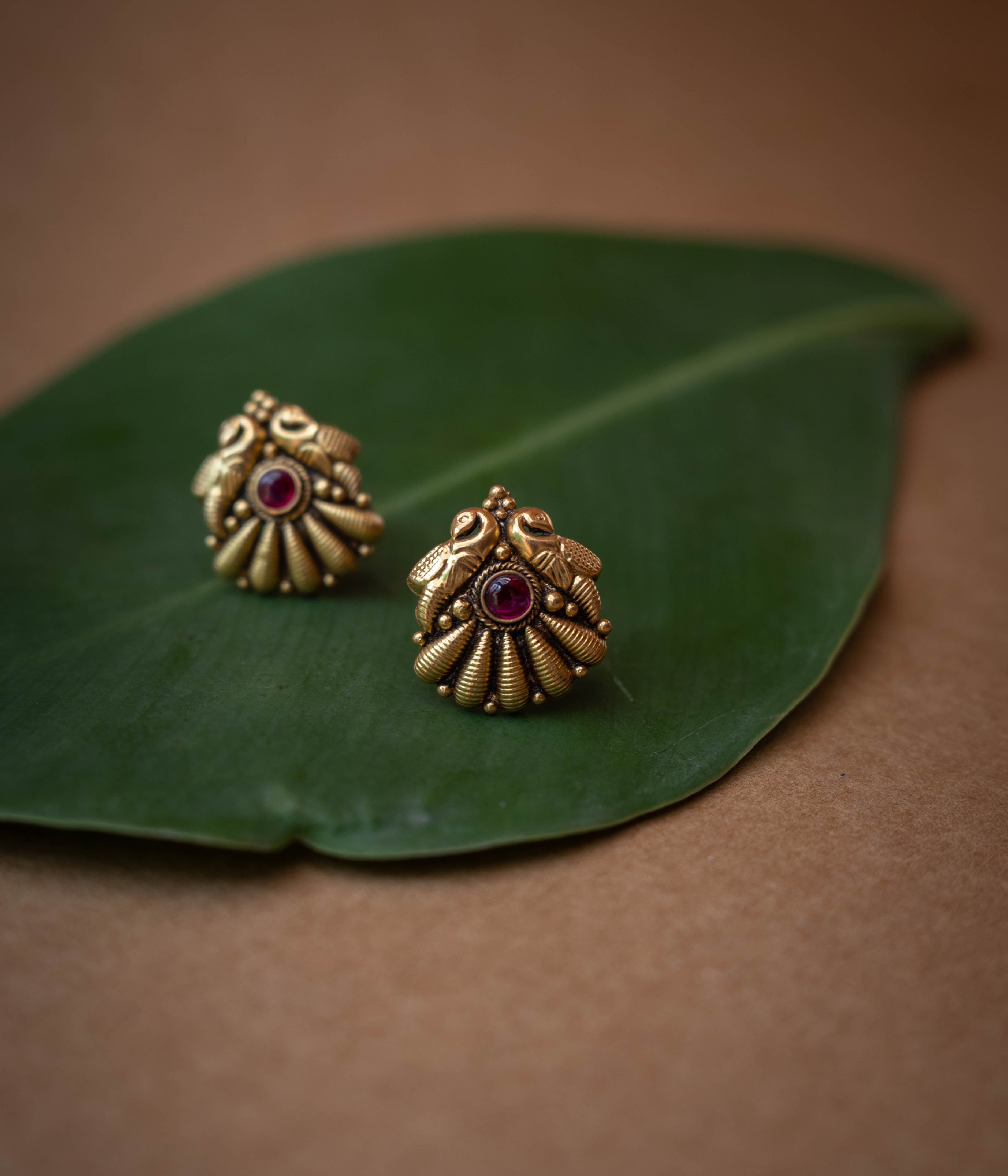 Traditional stud earrings with a central red stone and a stylized peacock and fan design.