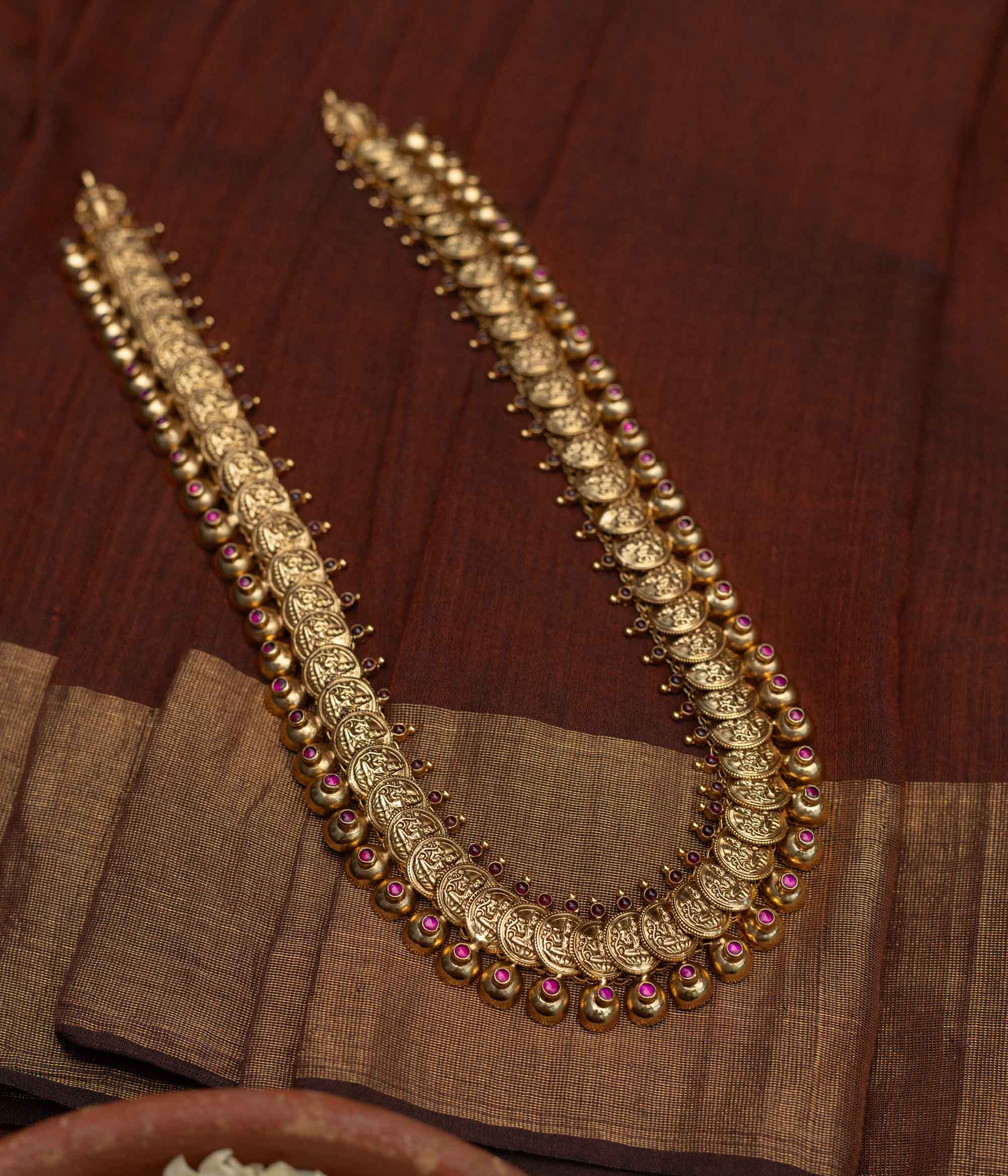 Long Kasu Mala necklace featuring an array of antique-finished gold (likely 92.5 sterling silver) coins depicting Goddess Lakshmi, delicately accented with ruby-toned stones, a timeless symbol of blessings and cultural richness.