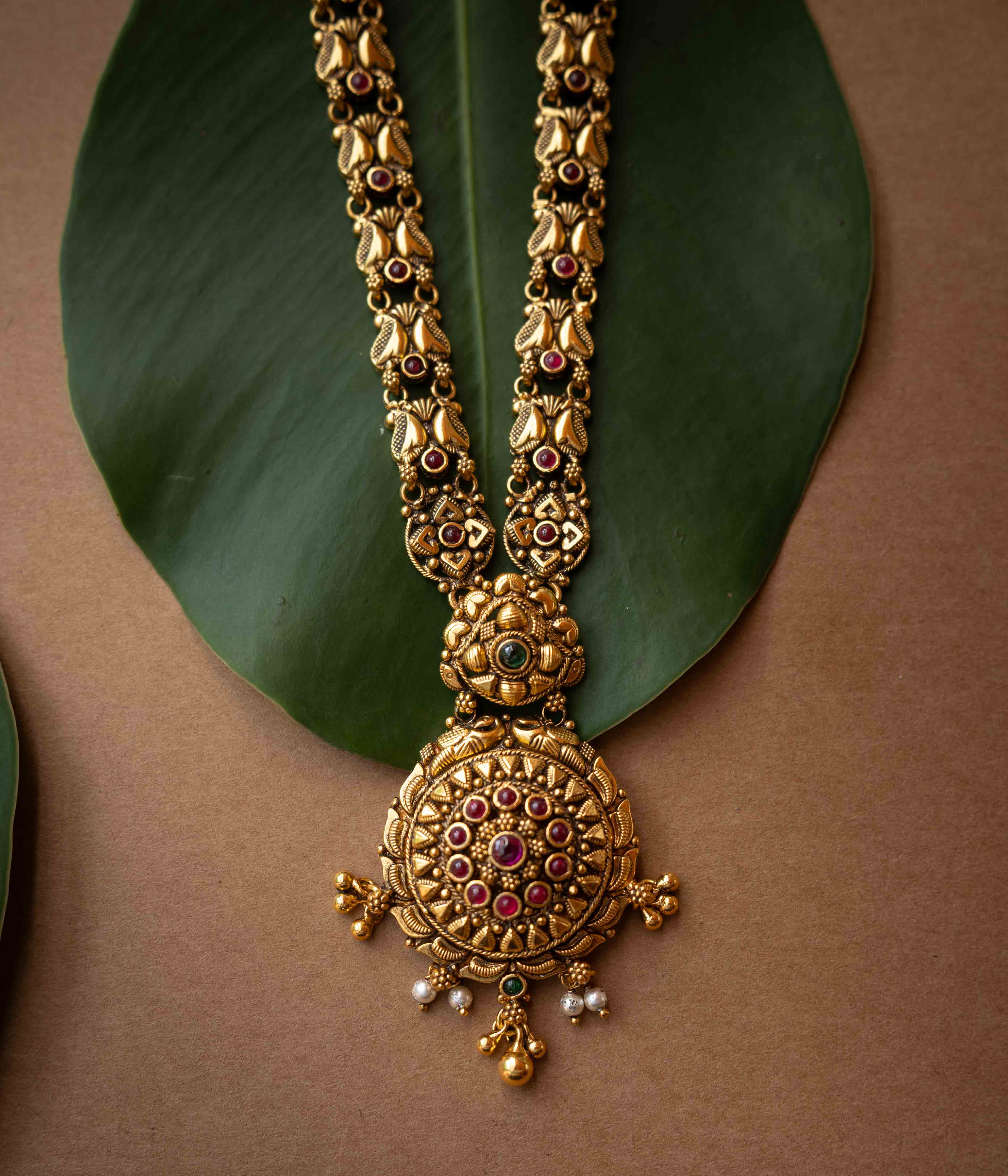 Antique gold temple necklace with lotus motifs and ruby-green stone accents from Temple Collection.

