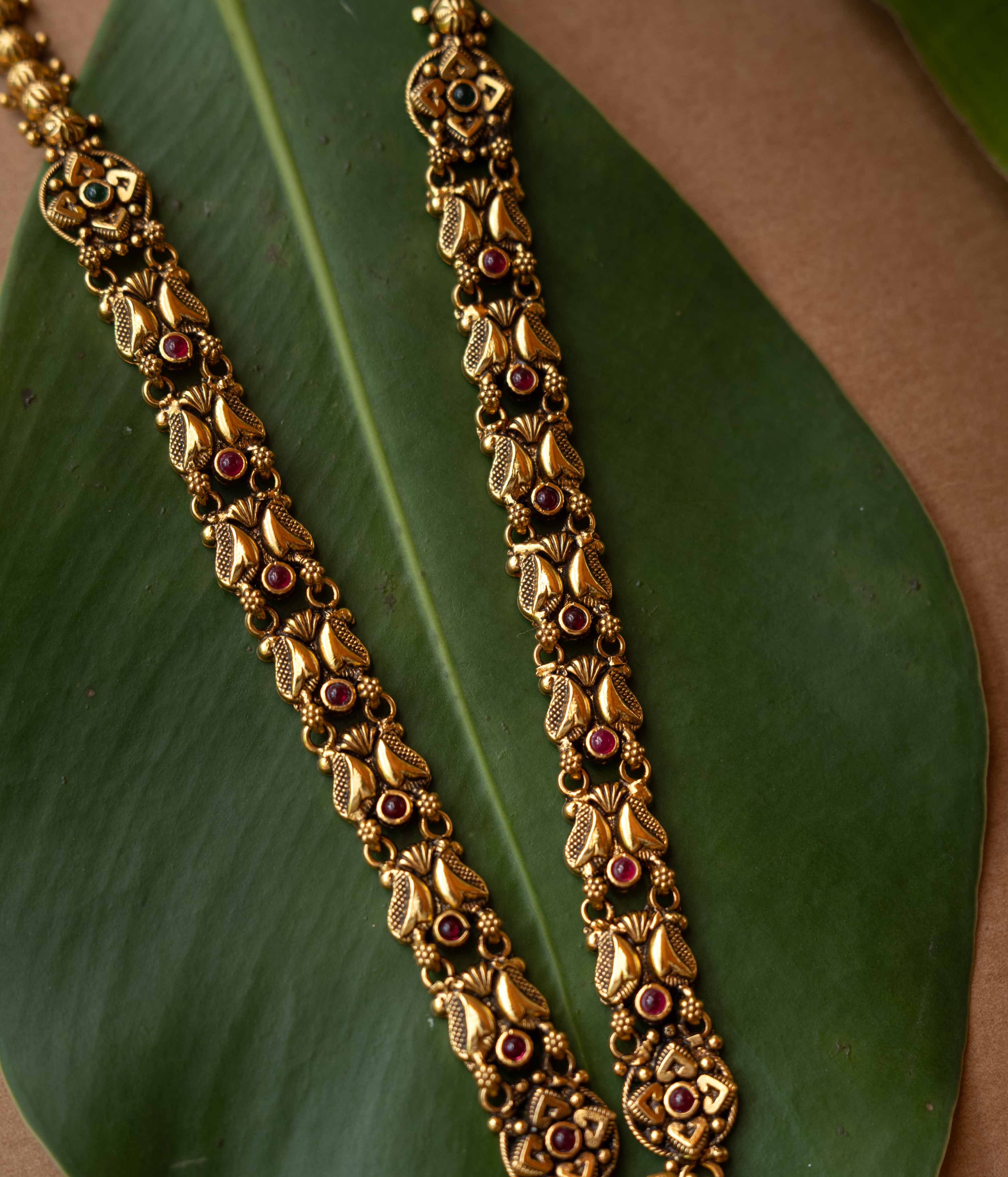 Antique gold temple necklace with lotus motifs and ruby-green stone accents from Temple Collection.
