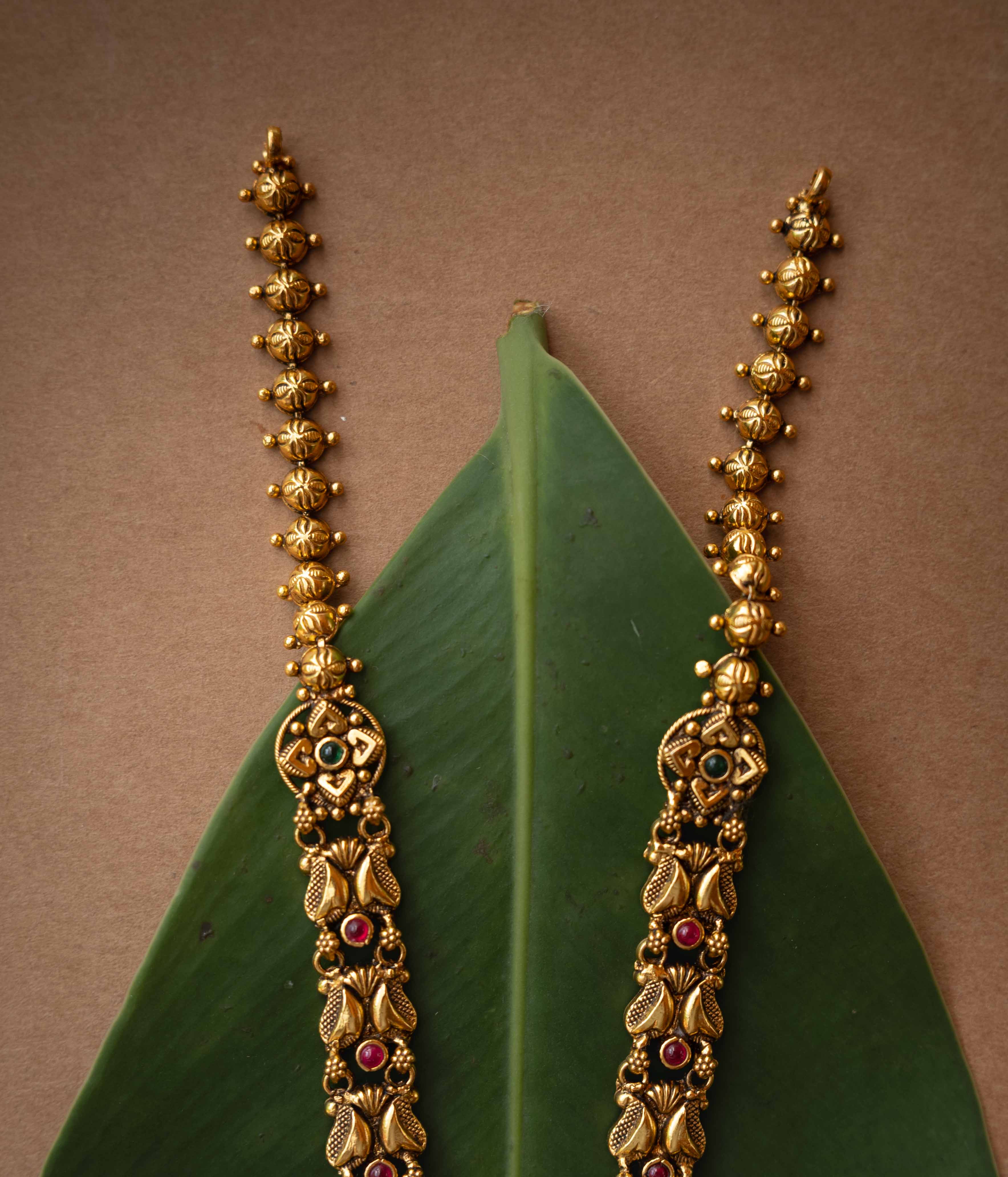 Antique gold temple necklace with lotus motifs and ruby-green stone accents from Temple Collection.
