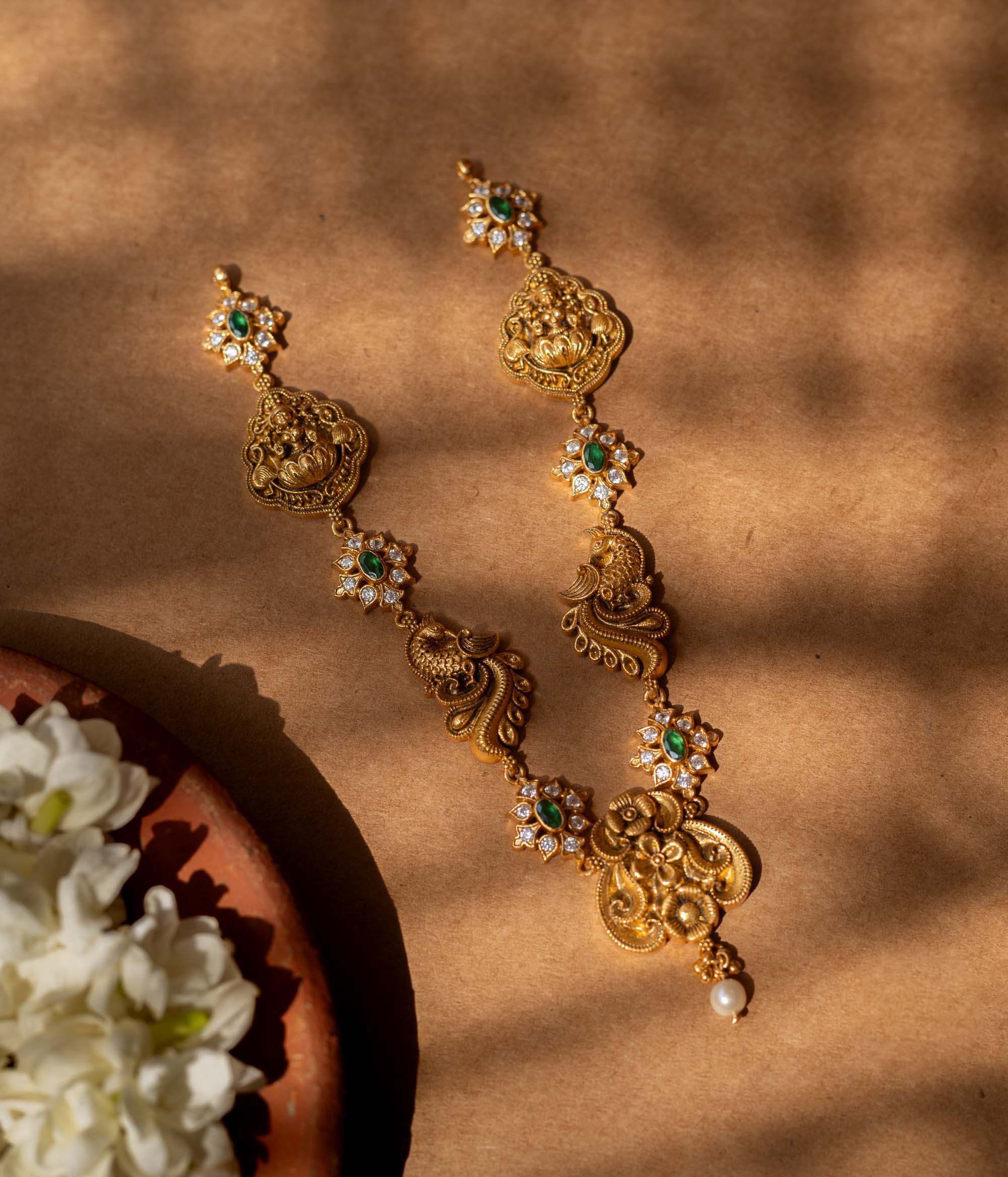 Antique gold-finished 92.5 sterling silver Peacock Devotion Antique Necklace featuring intricate Goddess Lakshmi and peacock motifs, adorned with shimmering green stones and delicate white crystals, reflecting traditional South Indian temple jewelry craftsmanship for festive occasions and weddings.