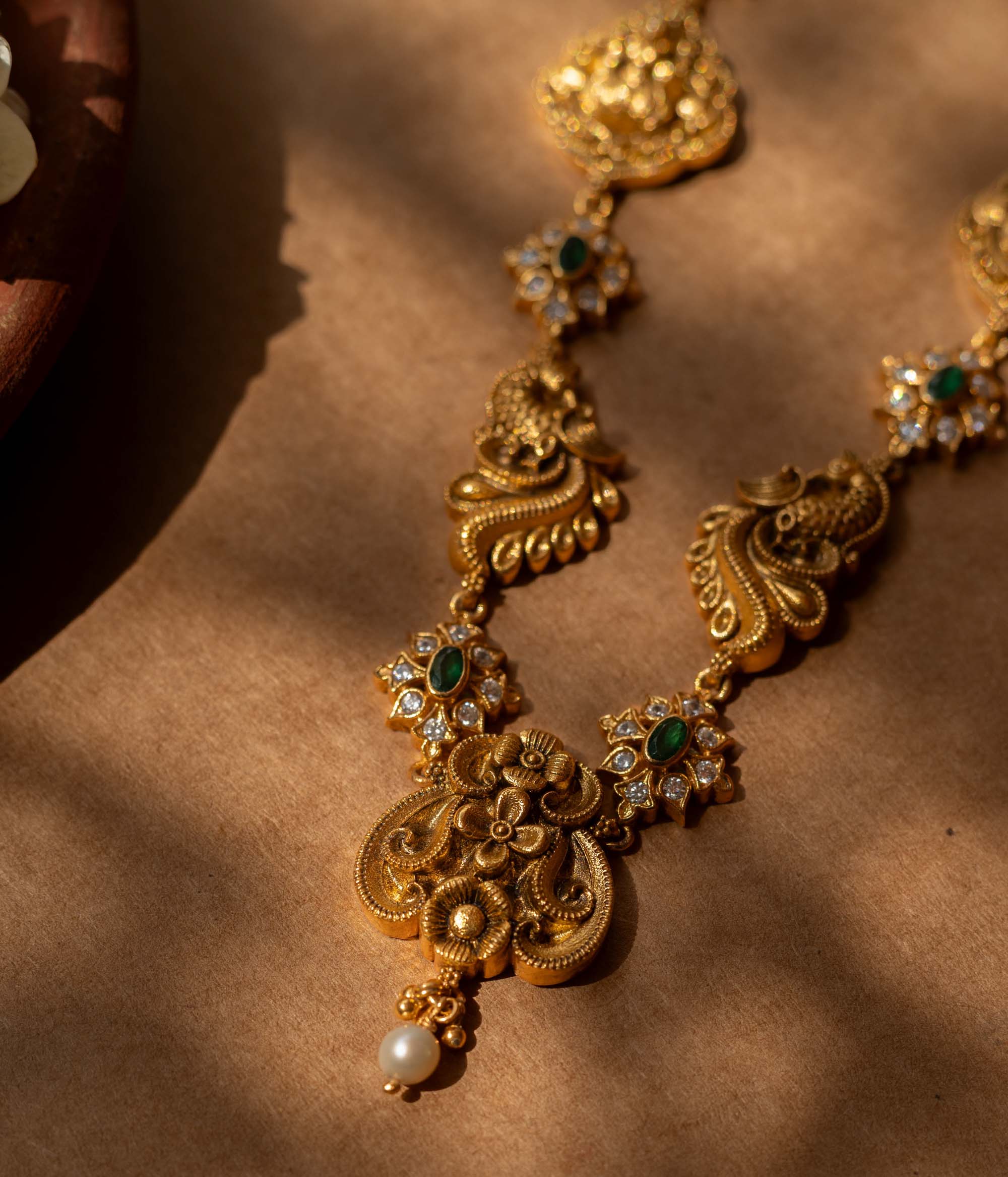 Antique gold-finished 92.5 sterling silver Peacock Devotion Antique Necklace featuring intricate Goddess Lakshmi and peacock motifs, adorned with shimmering green stones and delicate white crystals, reflecting traditional South Indian temple jewelry craftsmanship for festive occasions and weddings.