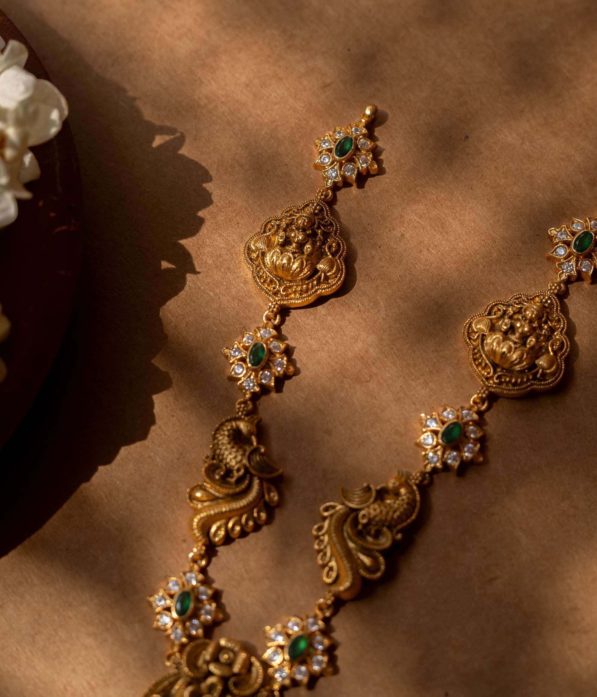 Antique gold-finished 92.5 sterling silver Peacock Devotion Antique Necklace featuring intricate Goddess Lakshmi and peacock motifs, adorned with shimmering green stones and delicate white crystals, reflecting traditional South Indian temple jewelry craftsmanship for festive occasions and weddings.
