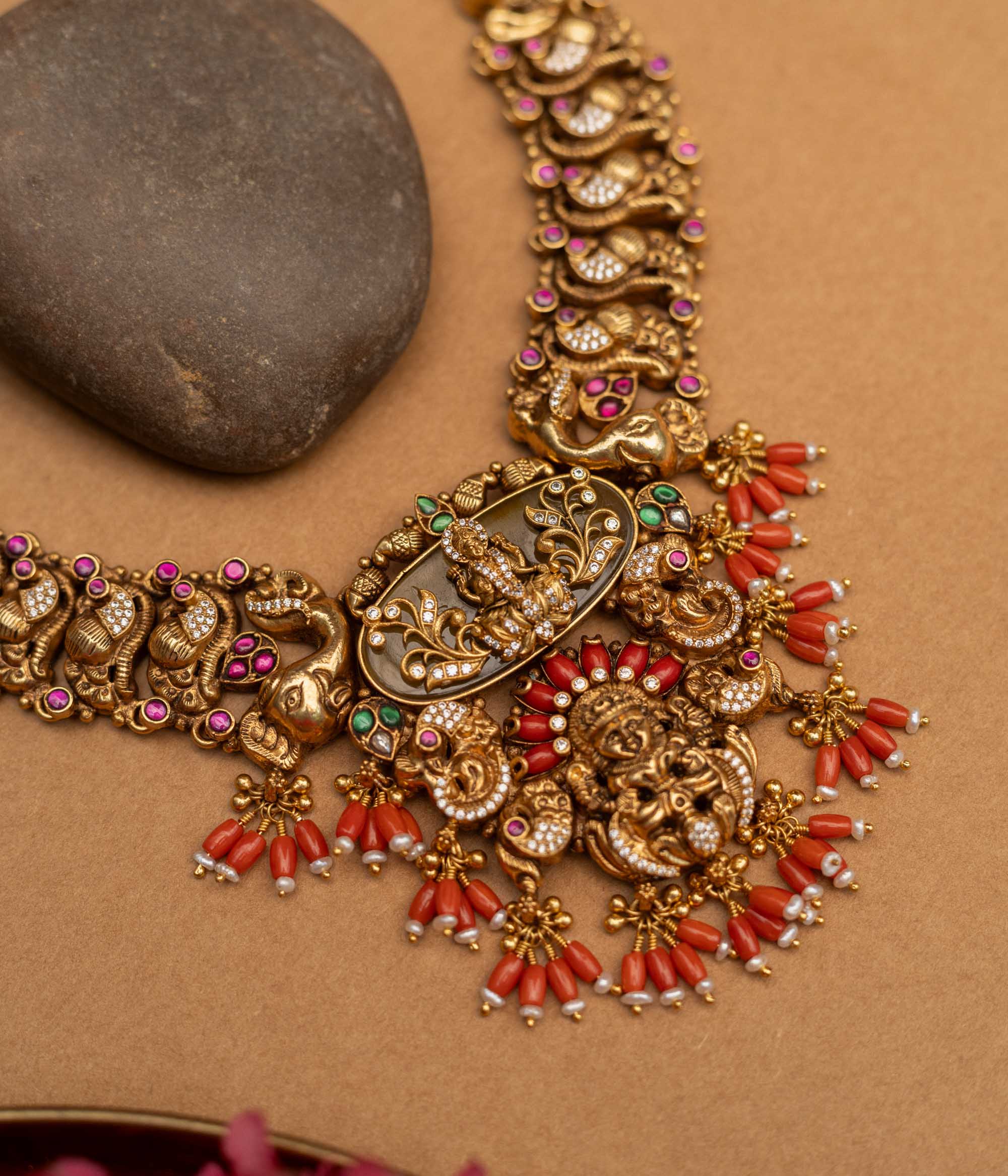 Elevate your traditional ensemble with the 92.5 sterling silver Divine Royal Heritage Choker, a magnificent piece of temple jewellery with an antique gold finish. This ornate choker features a central Lakshmi motif amidst intricate engravings, surrounded by elephants, peacocks, and mythological figures, accented with red coral drops, kundan stones, and delicate pearls, embodying spiritual grace and royal grandeur for weddings, poojas, and festive occasions.