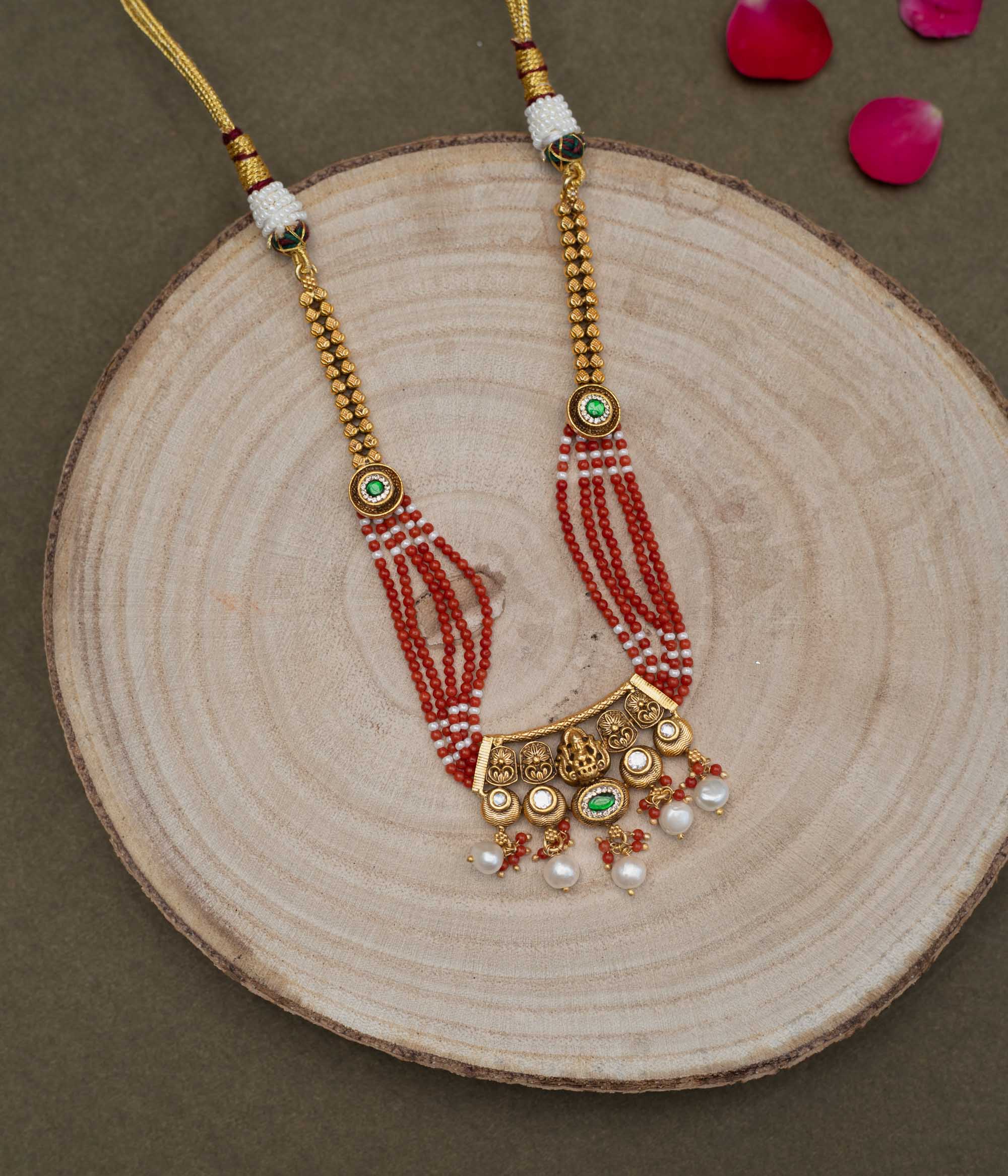 Multi-stranded necklace with vibrant coral and white beads, interspersed with gold-plated 92.5 sterling silver Ganesha motifs and green accents. Ganesha pendant with pearl drops.