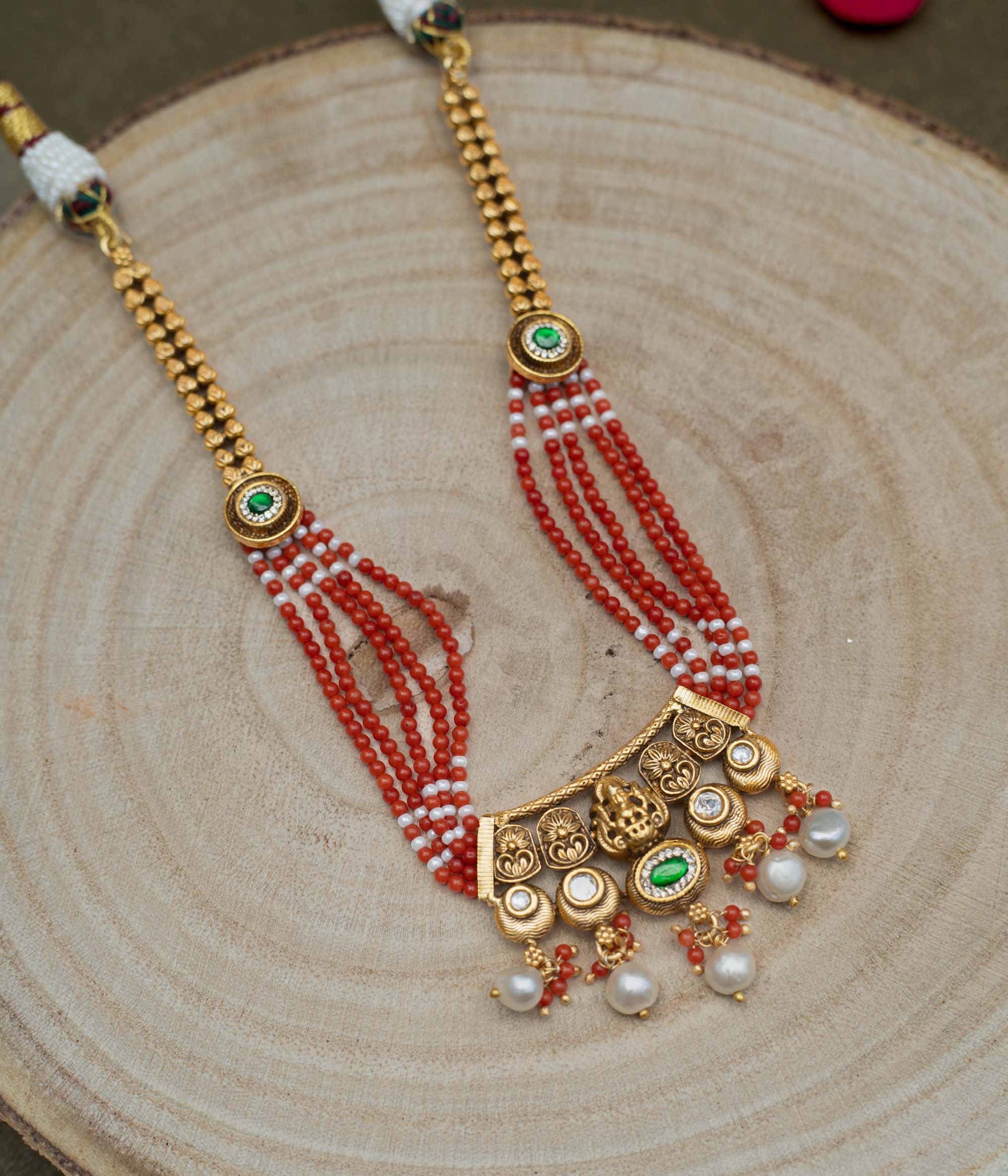 Multi-stranded necklace with vibrant coral and white beads, interspersed with gold-plated 92.5 sterling silver Ganesha motifs and green accents. Ganesha pendant with pearl drops.
