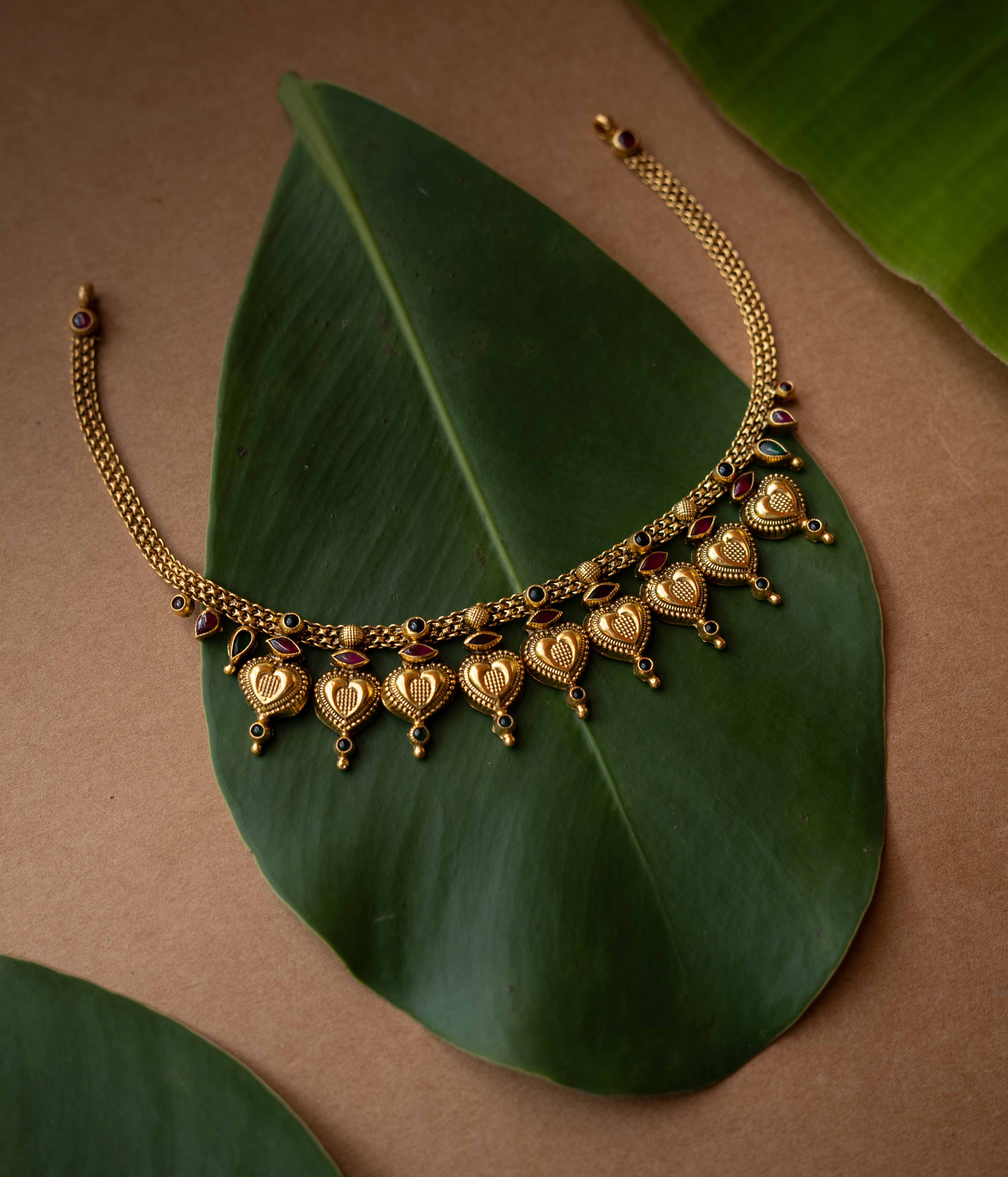 Antique gold temple necklace with heart-shaped motifs and ruby-green accents from Temple Collection.