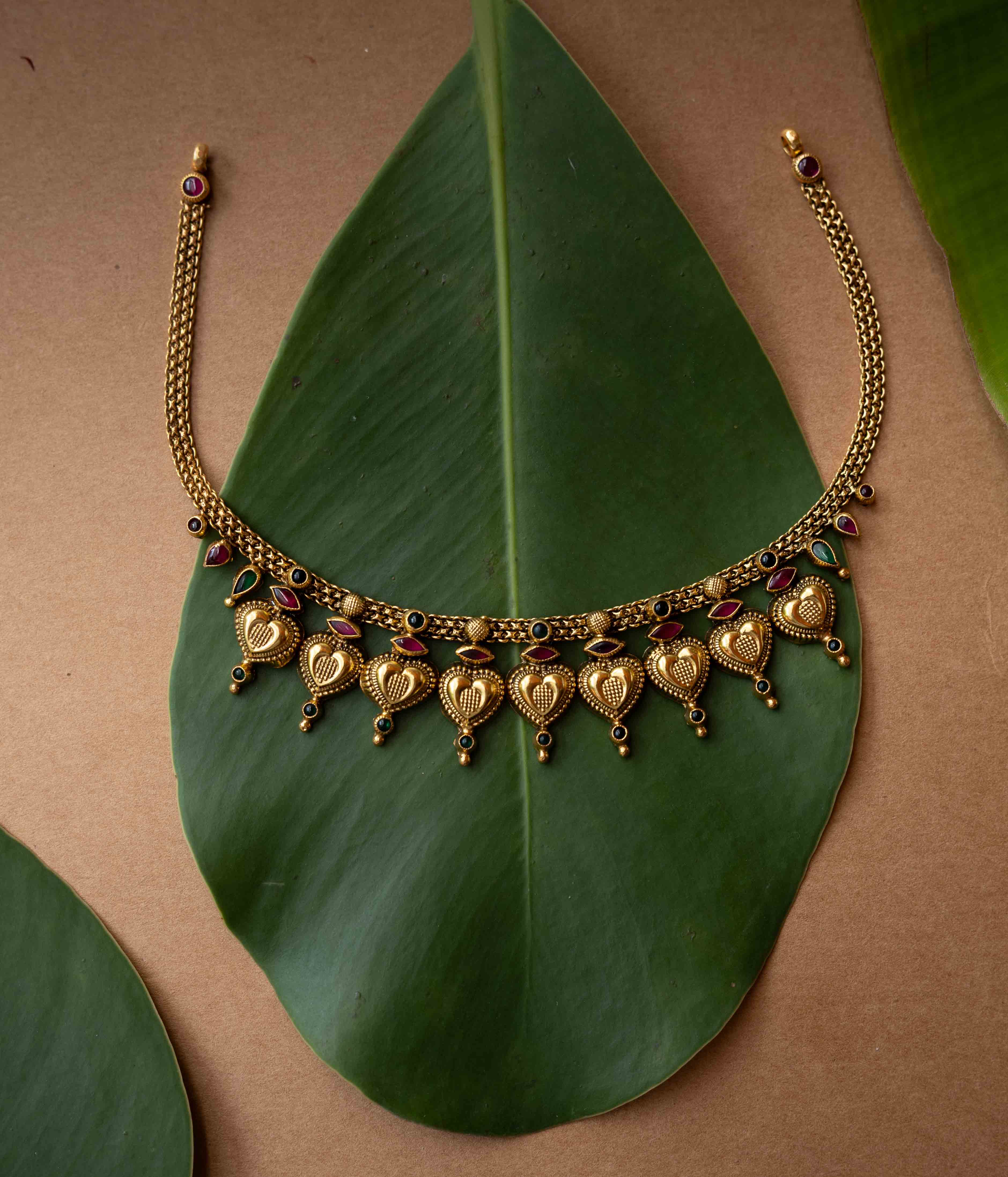 Antique gold temple necklace with heart-shaped motifs and ruby-green accents from Temple Collection.