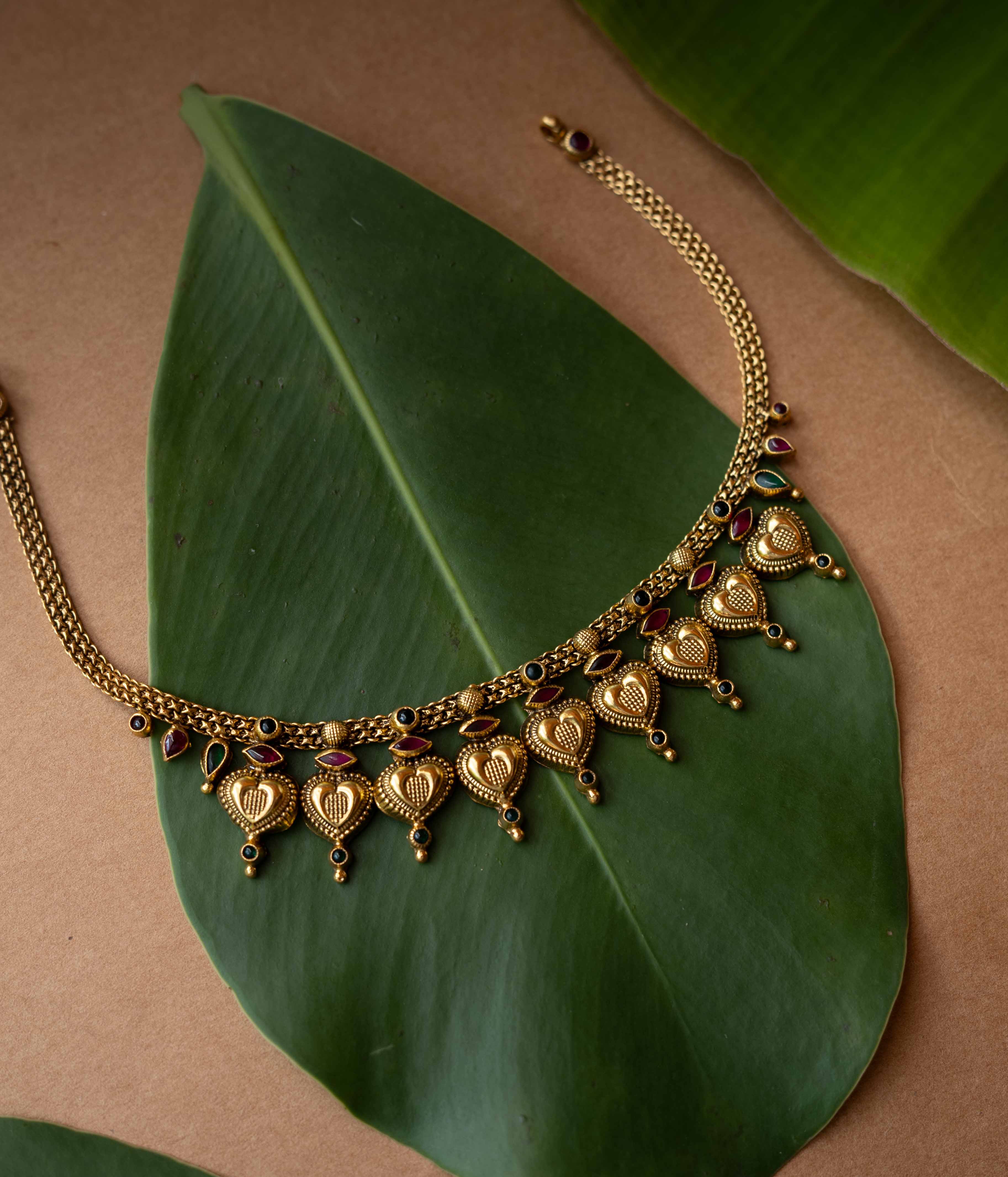 Antique gold temple necklace with heart-shaped motifs and ruby-green accents from Temple Collection.