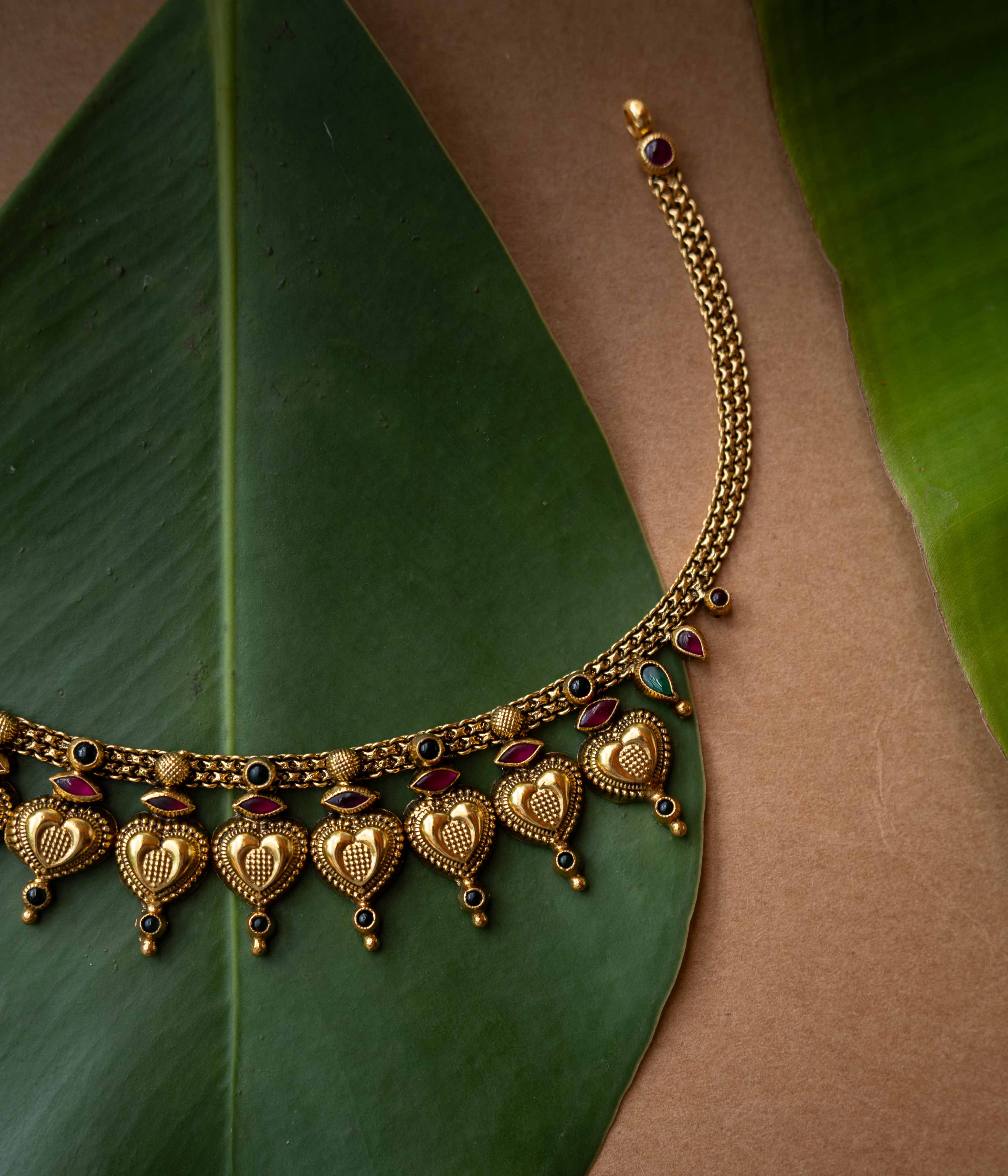 Antique gold temple necklace with heart-shaped motifs and ruby-green accents from Temple Collection.