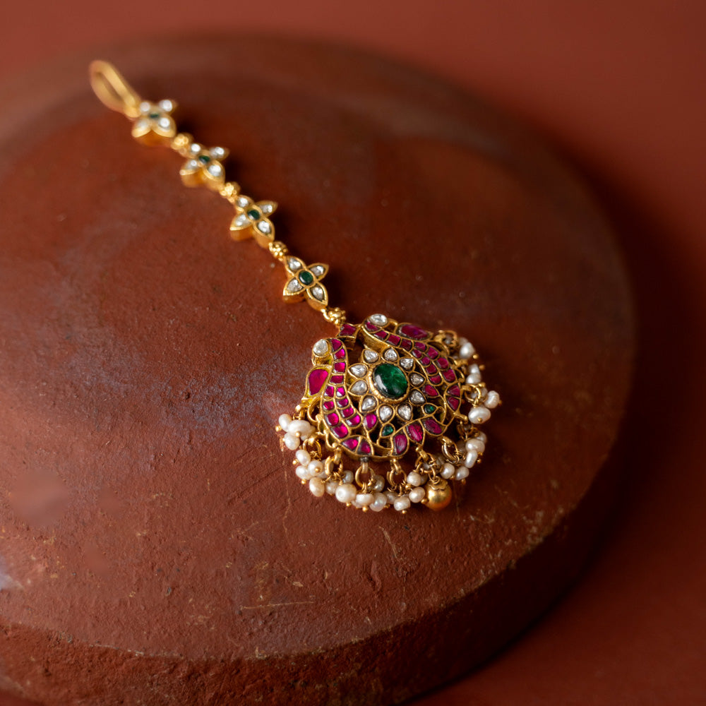 A handcrafted 92.5 sterling silver and 22ct gold-plated Kundan tikka, featuring red, green, and white Kundan stones and pearls, adorned with intricate gold detailing and capturing the essence of royal charm.