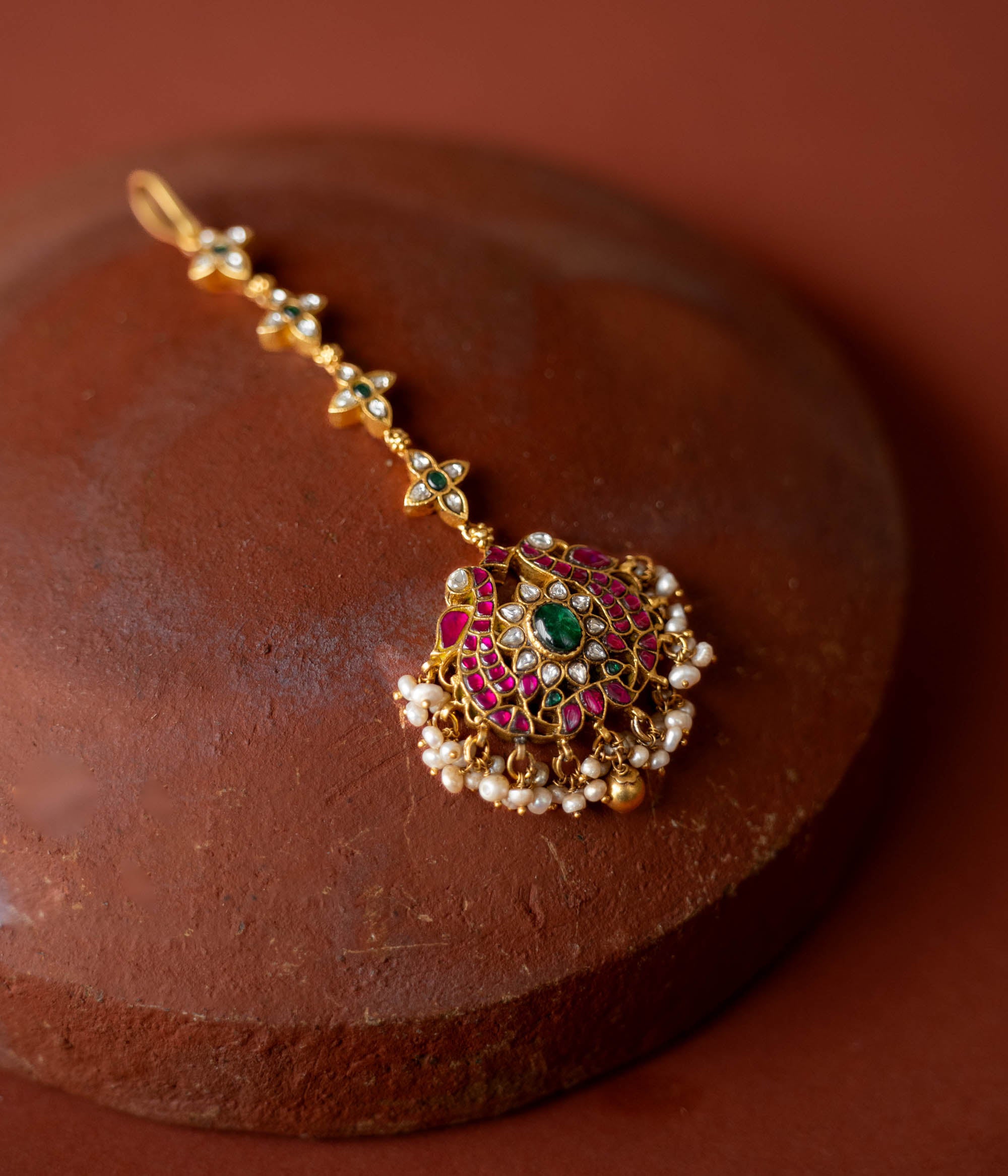 A handcrafted 92.5 sterling silver and 22ct gold-plated Kundan tikka, featuring red, green, and white Kundan stones and pearls, adorned with intricate gold detailing and capturing the essence of royal charm.