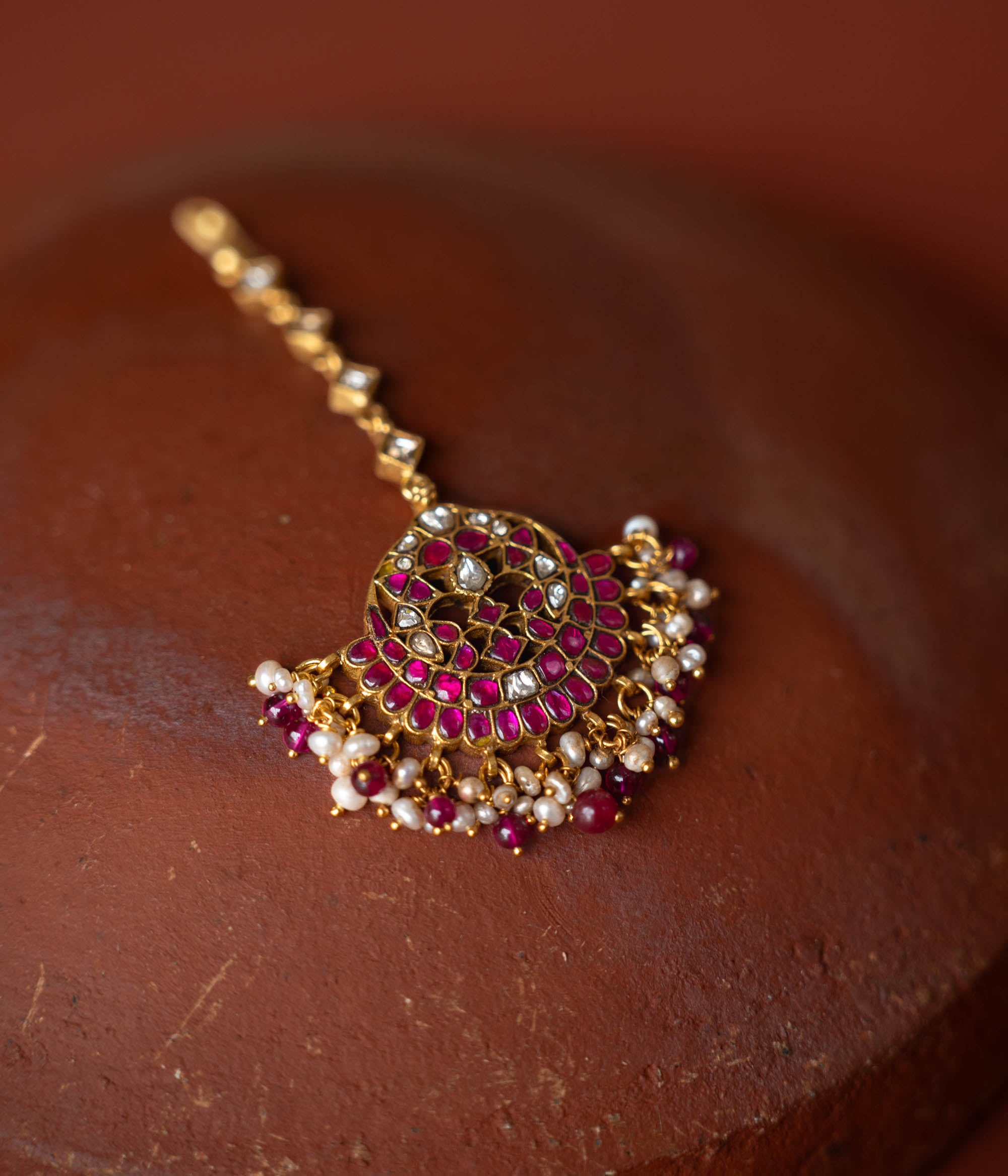 A handcrafted 92.5 sterling silver and 22ct gold-plated Kundan tikka, adorned with red, green, and white Kundan stones, red beads, and pearls, featuring intricate gold detailing and embodying divine grace and timeless elegance.