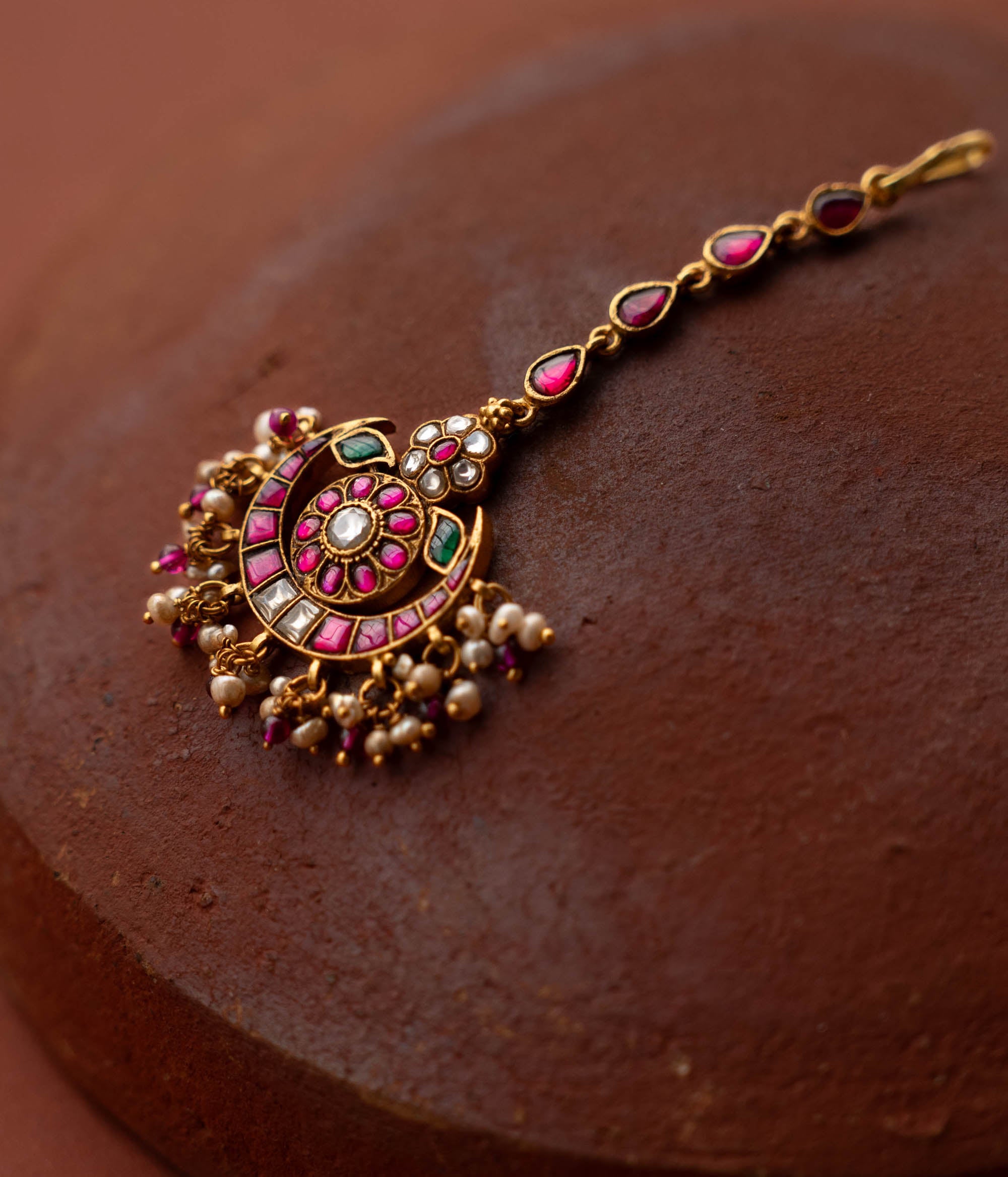 A handcrafted 92.5 sterling silver and 22ct gold-plated Kundan tikka, featuring red, green, and white Kundan stones and pearls, with intricate gold detailing, inspired by the glow of the moon and radiating celestial grace and timeless charm.