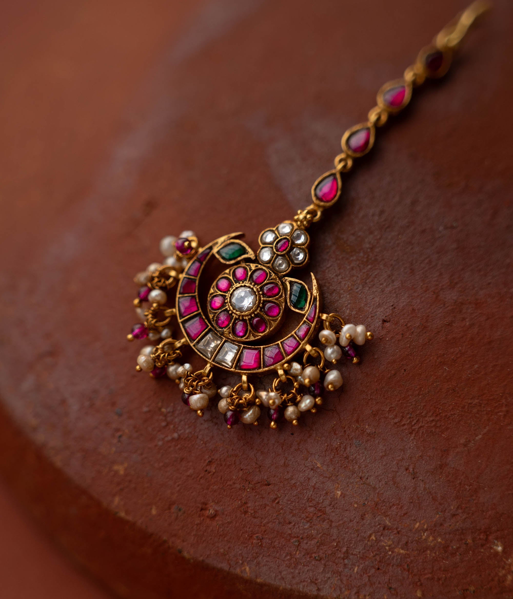 A handcrafted 92.5 sterling silver and 22ct gold-plated Kundan tikka, featuring red, green, and white Kundan stones and pearls, with intricate gold detailing, inspired by the glow of the moon and radiating celestial grace and timeless charm.