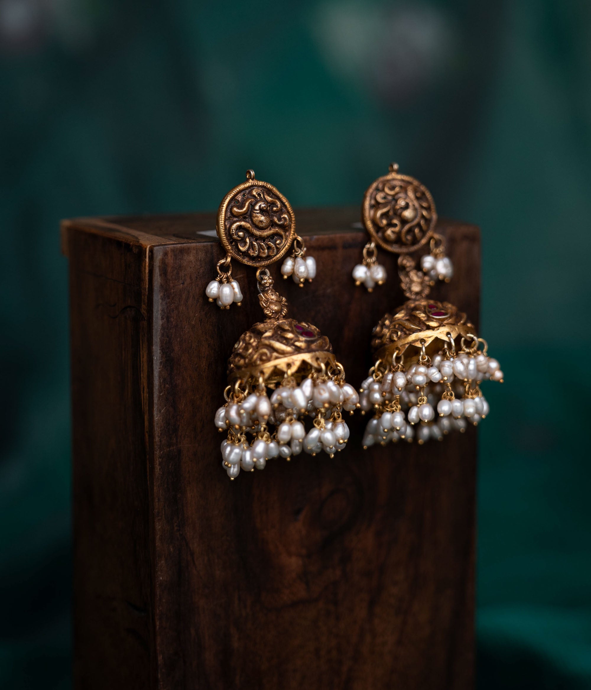 A pair of 92.5 sterling silver earrings with screw fastenings, featuring red Kundan stones and pearls, showcasing intricate temple-inspired carvings, antique gold detailing, and embodying divine elegance.