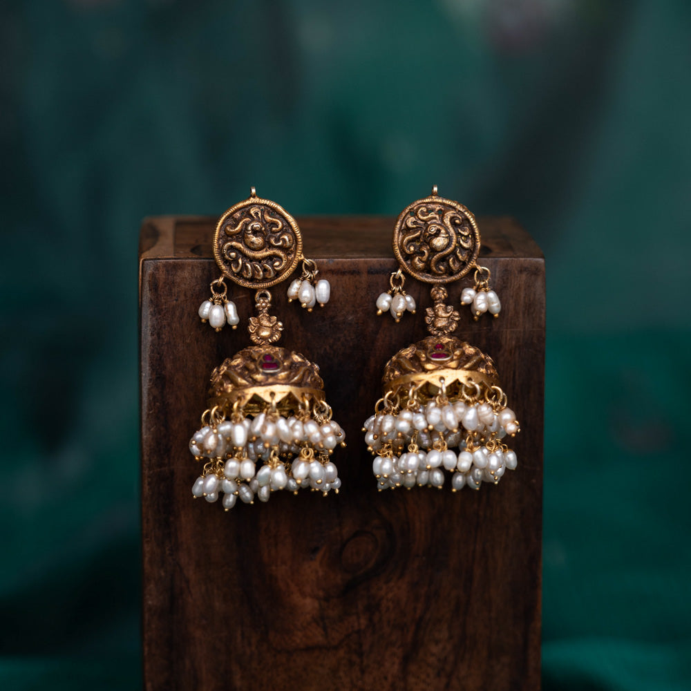 A pair of 92.5 sterling silver earrings with screw fastenings, featuring red Kundan stones and pearls, showcasing intricate temple-inspired carvings, antique gold detailing, and embodying divine elegance.