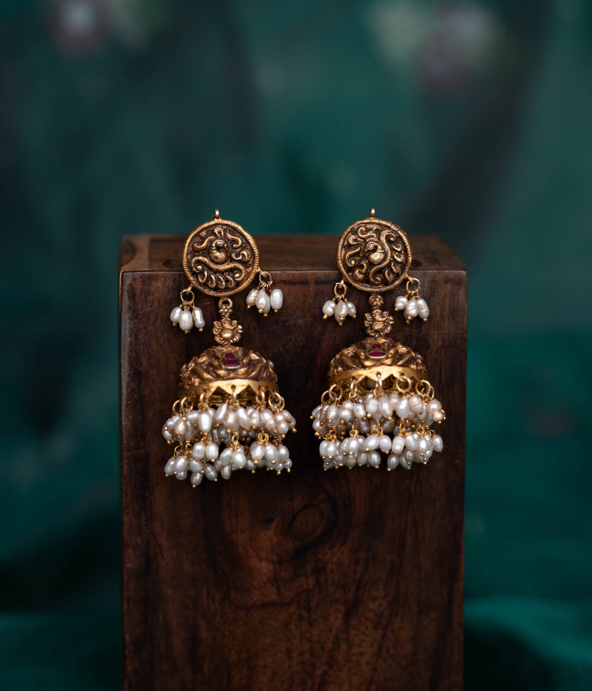 A pair of 92.5 sterling silver earrings with screw fastenings, featuring red Kundan stones and pearls, showcasing intricate temple-inspired carvings, antique gold detailing, and embodying divine elegance.