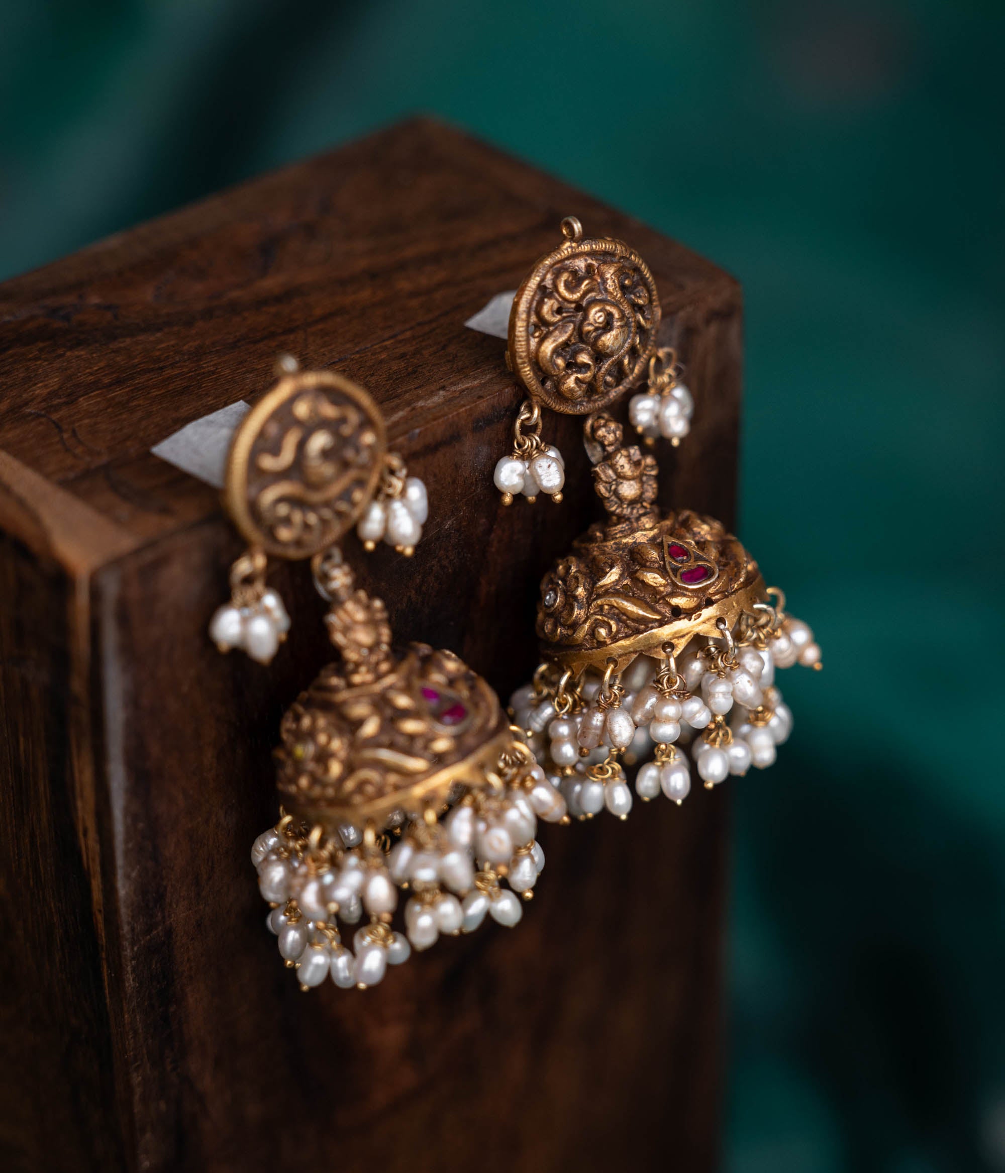 A pair of 92.5 sterling silver earrings with screw fastenings, featuring red Kundan stones and pearls, showcasing intricate temple-inspired carvings, antique gold detailing, and embodying divine elegance.