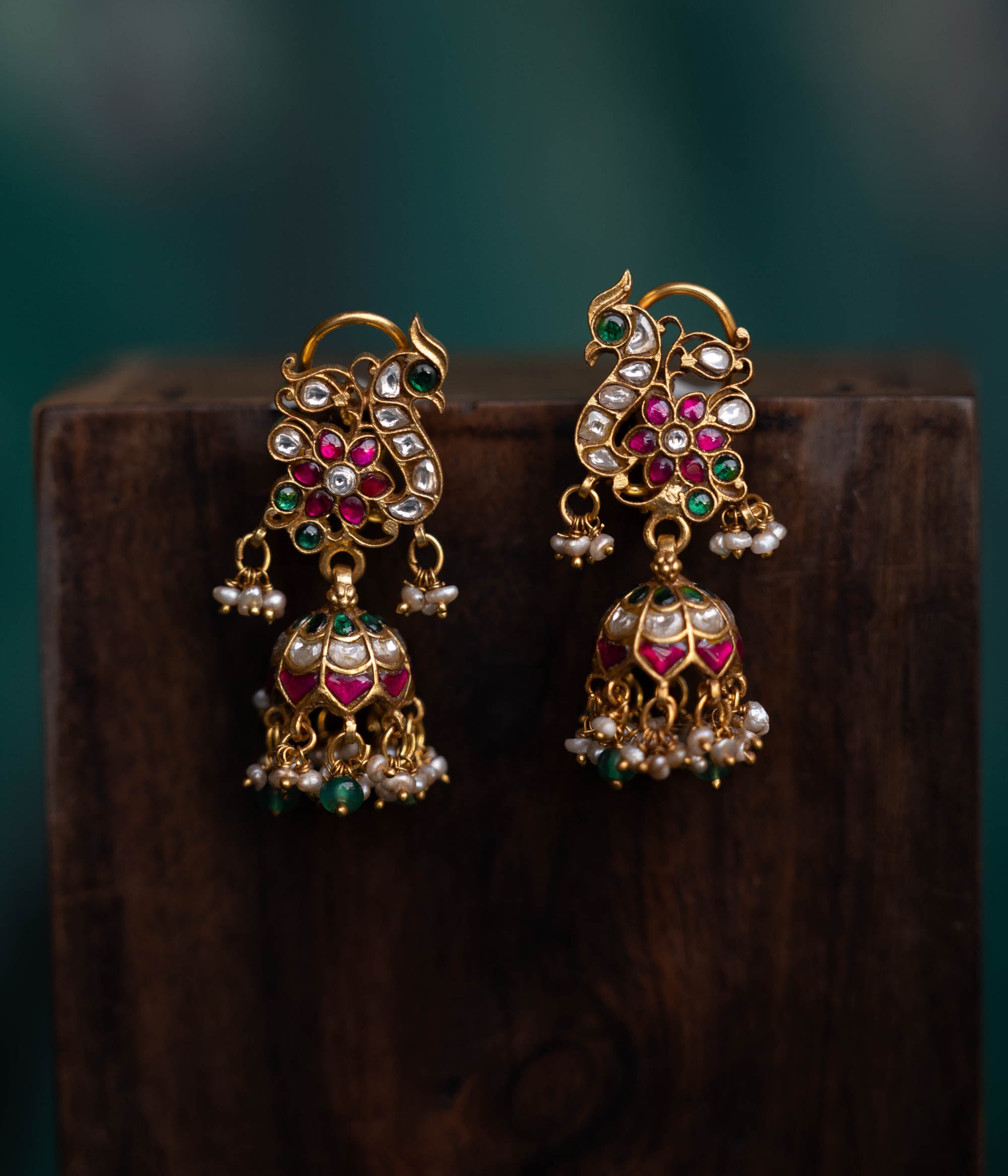 A pair of handcrafted 92.5 sterling silver earrings with screw fastenings, featuring a regal peacock motif adorned with red, white, and green Kundan stones, green beads, and pearls, showcasing intricate gold detailing and capturing the essence of grace and tradition.