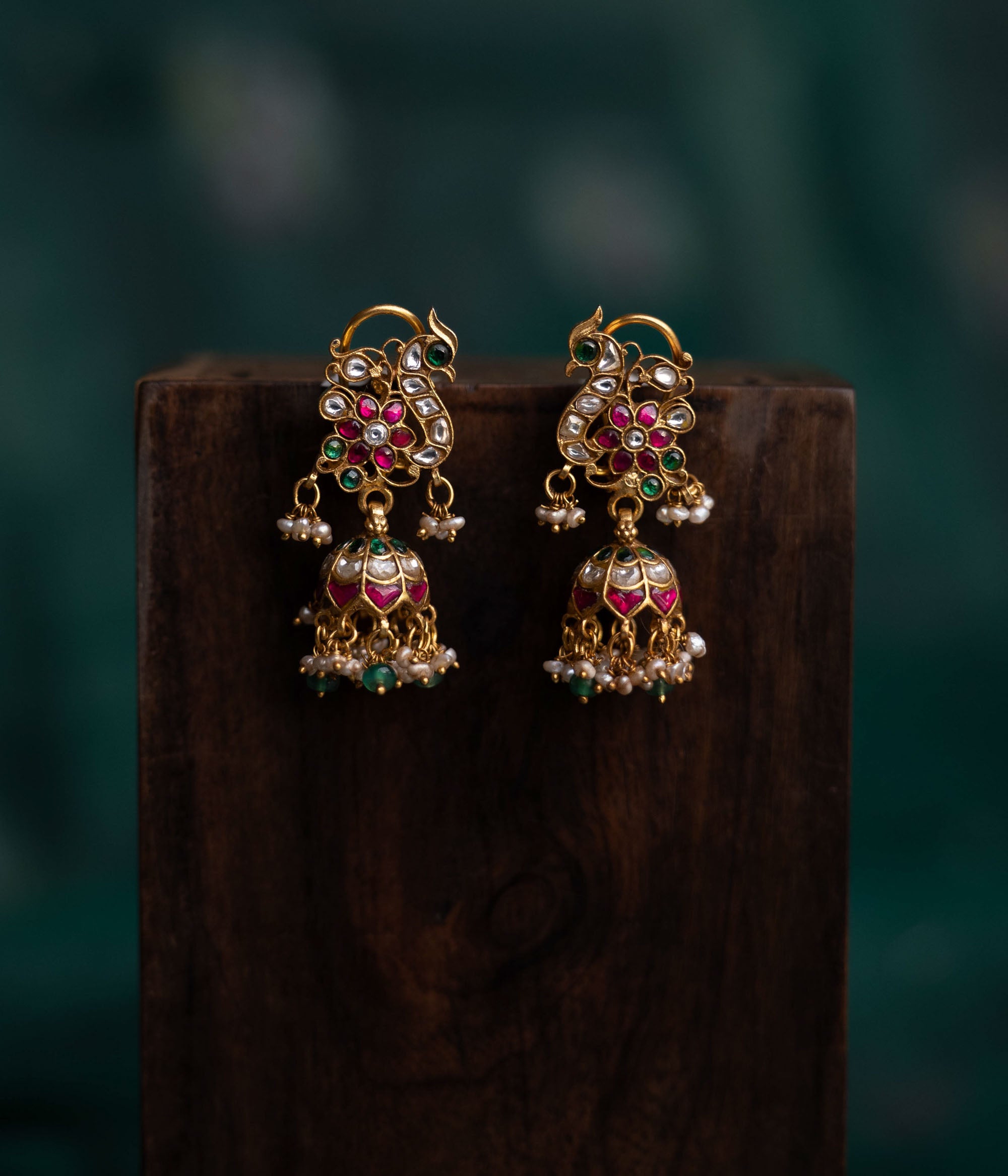 A pair of handcrafted 92.5 sterling silver earrings with screw fastenings, featuring a regal peacock motif adorned with red, white, and green Kundan stones, green beads, and pearls, showcasing intricate gold detailing and capturing the essence of grace and tradition.