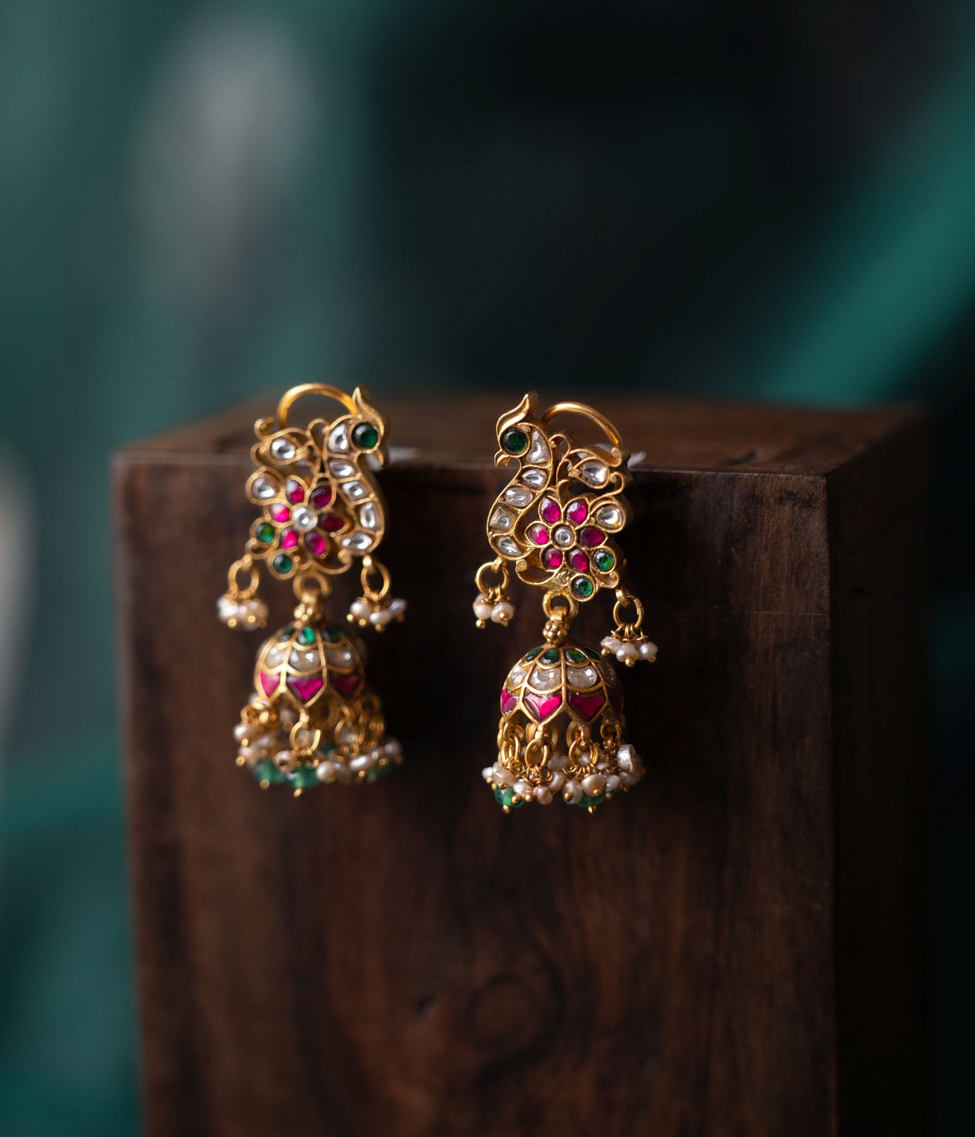 A pair of handcrafted 92.5 sterling silver earrings with screw fastenings, featuring a regal peacock motif adorned with red, white, and green Kundan stones, green beads, and pearls, showcasing intricate gold detailing and capturing the essence of grace and tradition.