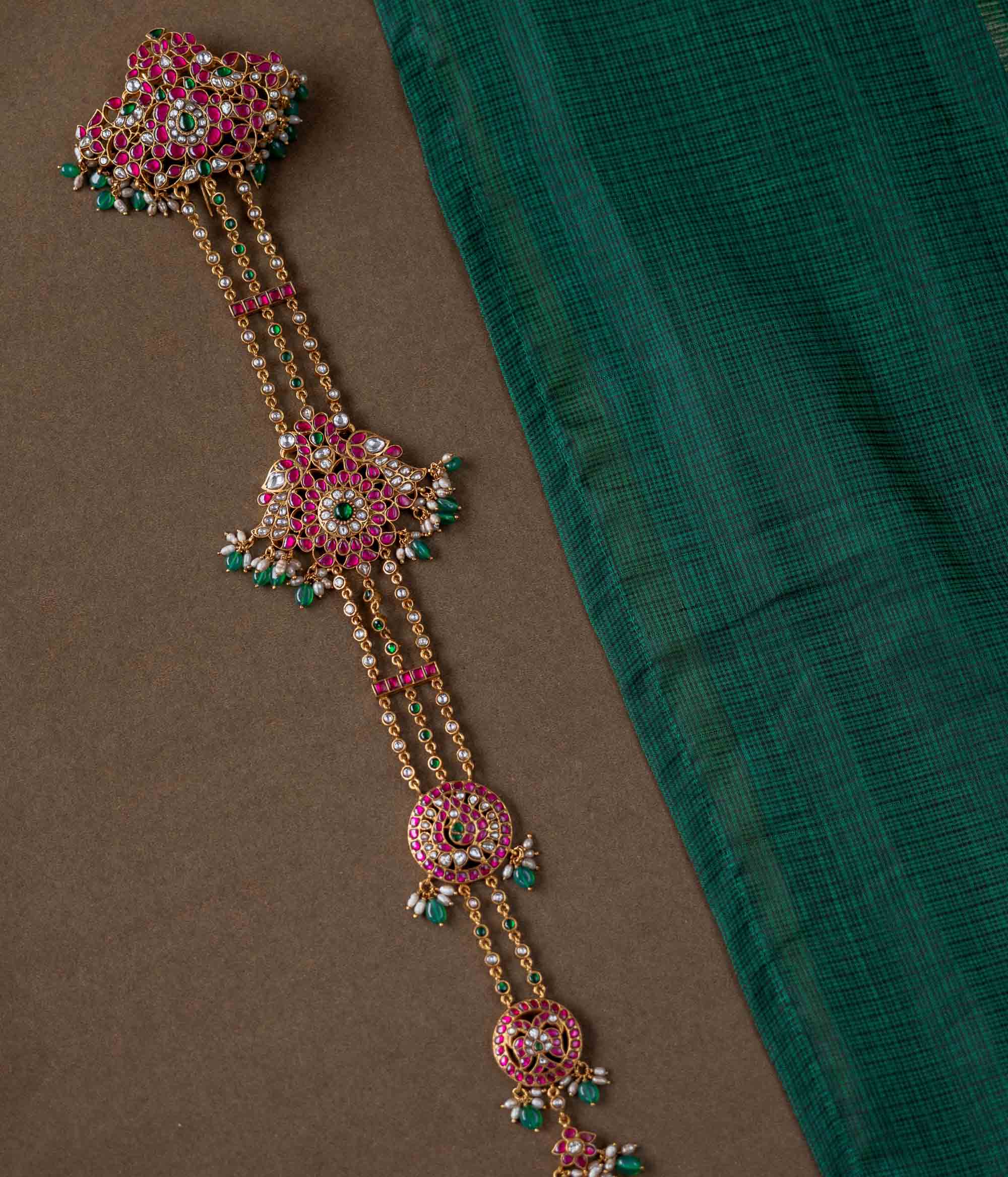 A handcrafted 92.5 sterling silver hair ornament (jadai) featuring red, green, and white Kundan stones, green beads, and pearls, adding a regal touch to bridal and traditional wear.