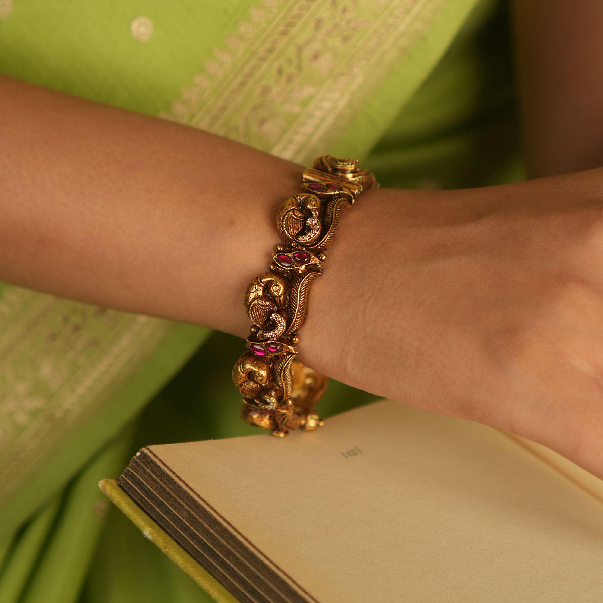 Antique gold-plated bangle with peacock motifs and pink kundan stones.