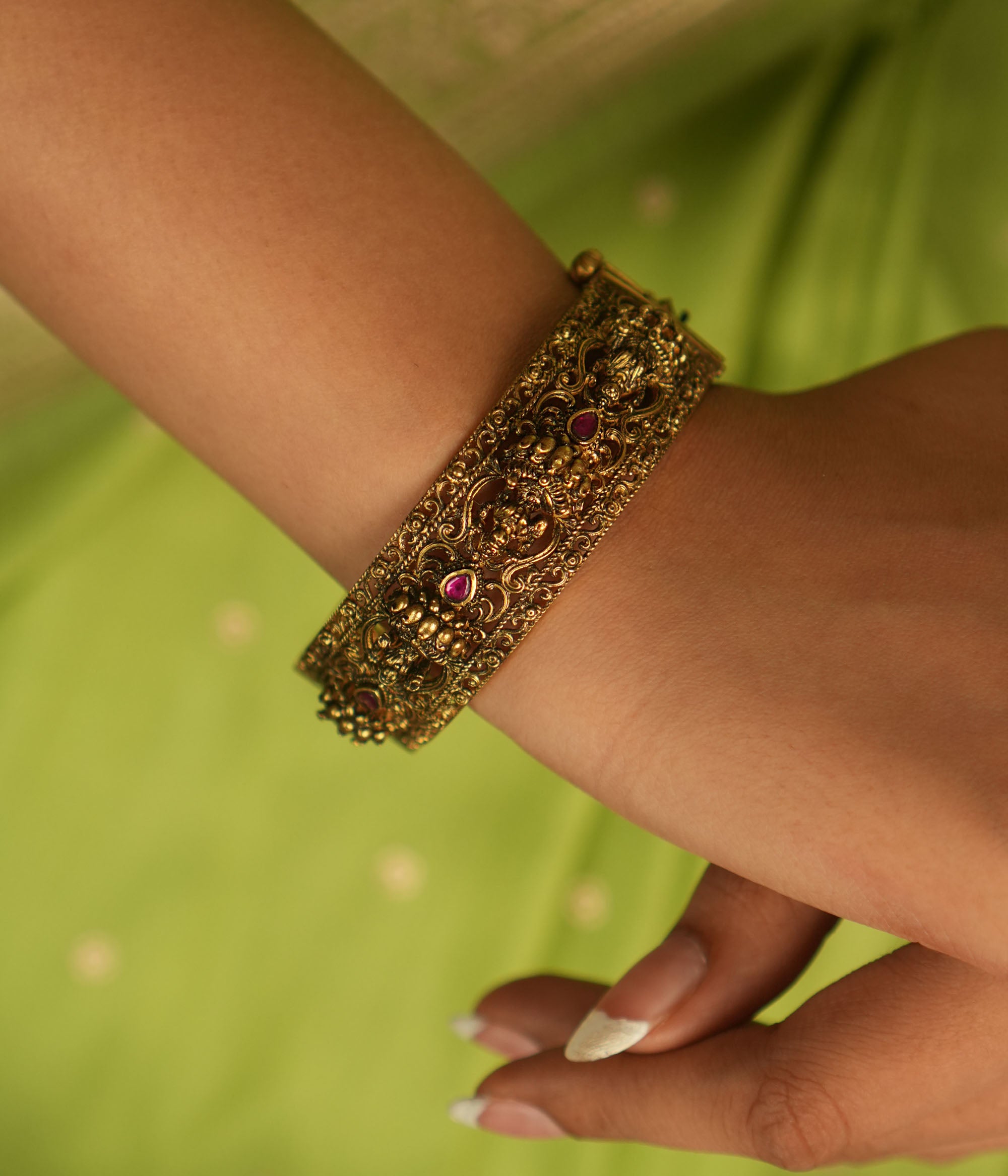 Antique gold bangle featuring Lakshmi motifs adorned with pink kundan stones, a timeless temple-inspired treasure.