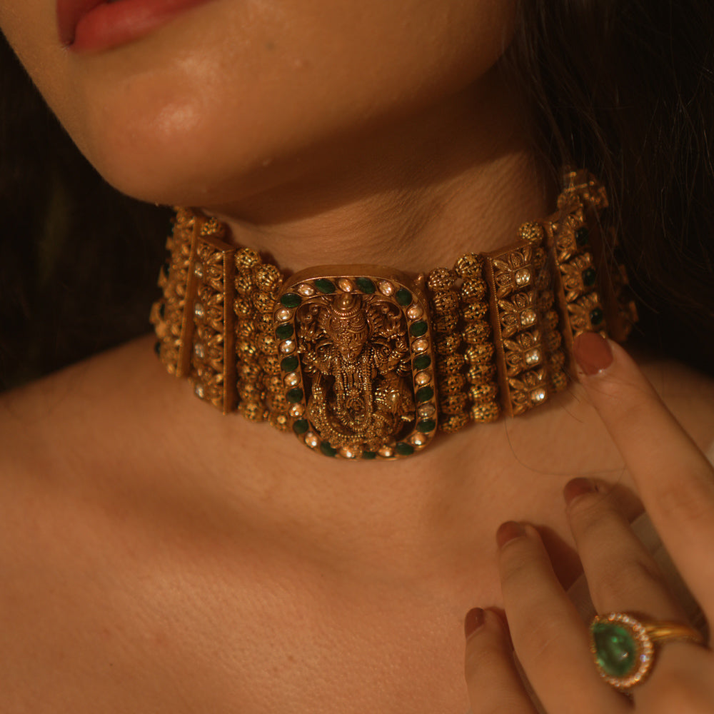 Temple collection Alyaa Necklace featuring Goddess Lakshmi, floral carvings, and emerald green Kundan stones in a choker design.