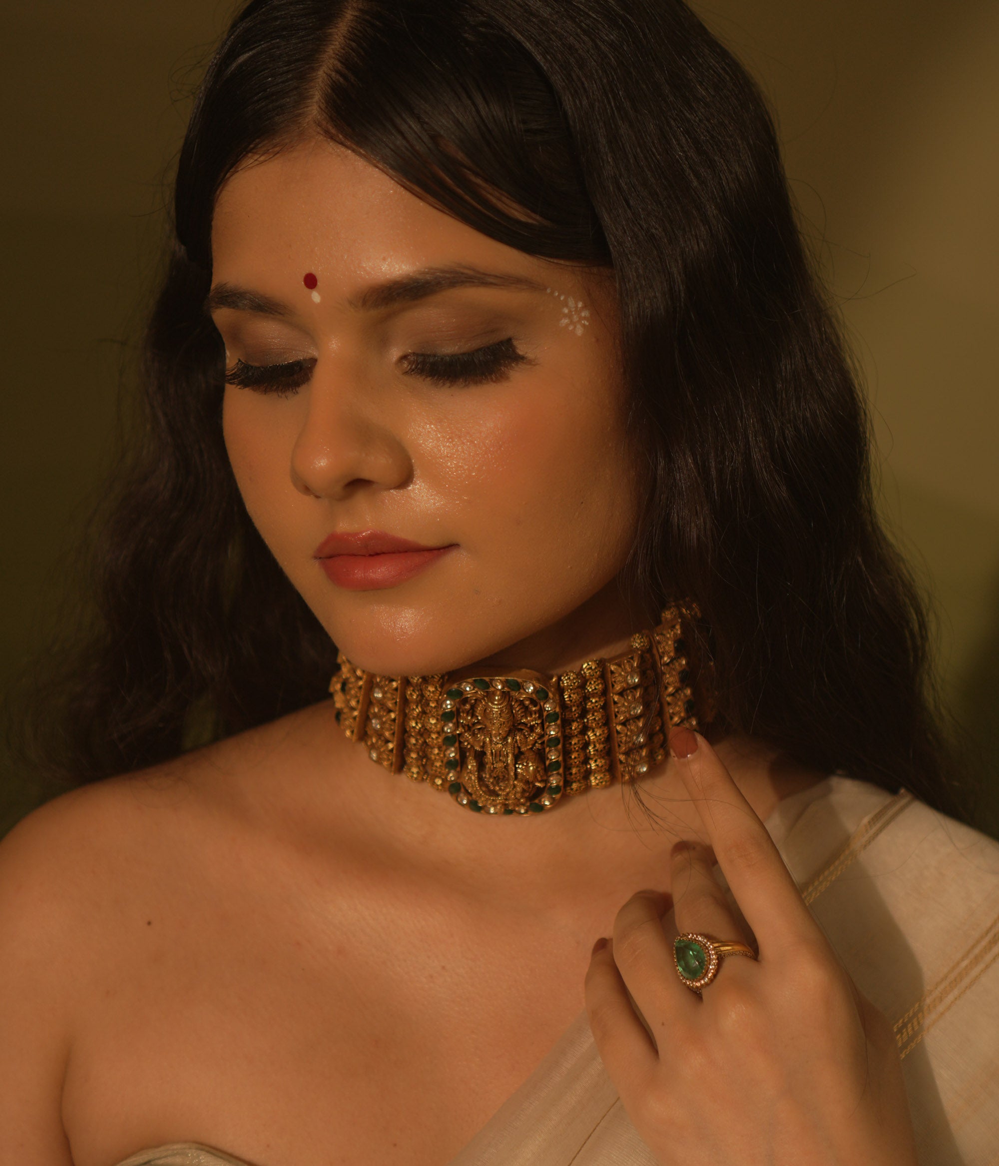 Temple collection Alyaa Necklace featuring Goddess Lakshmi, floral carvings, and emerald green Kundan stones in a choker design.